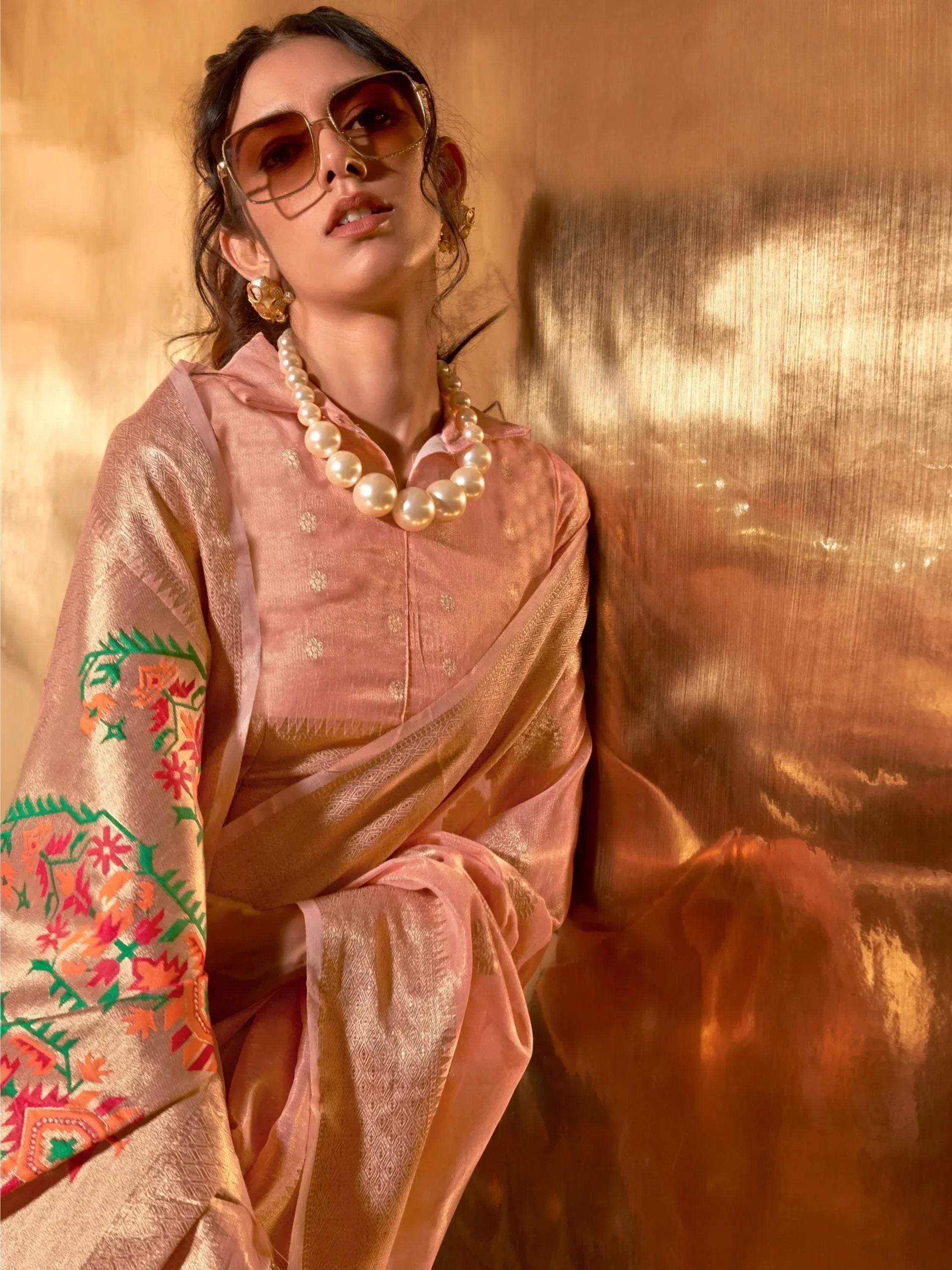 Woman in pink embroidered ethnic saree with pearl necklace and sunglasses, golden backdrop