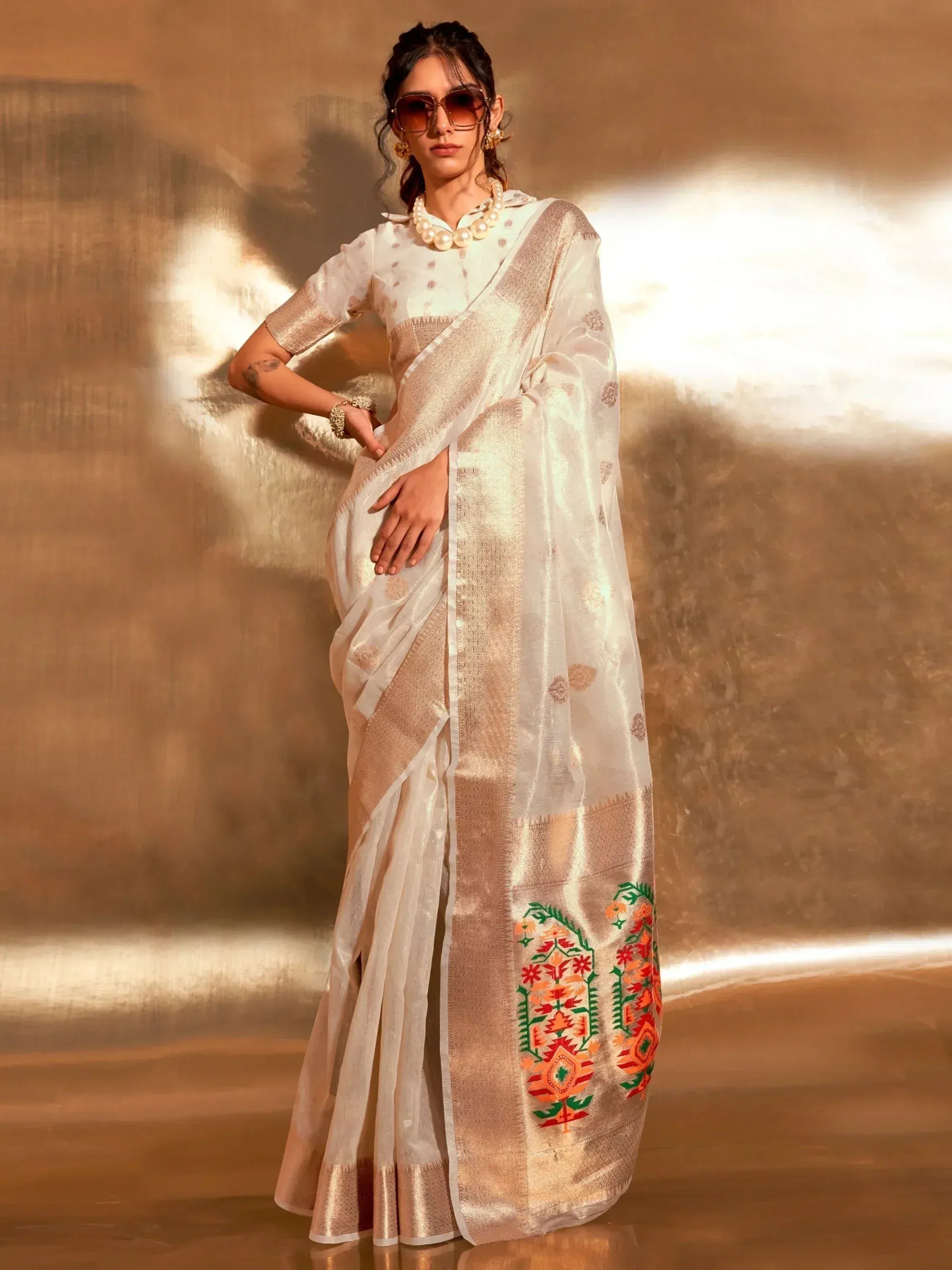 Elegant white saree with floral embroidery and golden border, paired with pearl necklace and sunglasses.