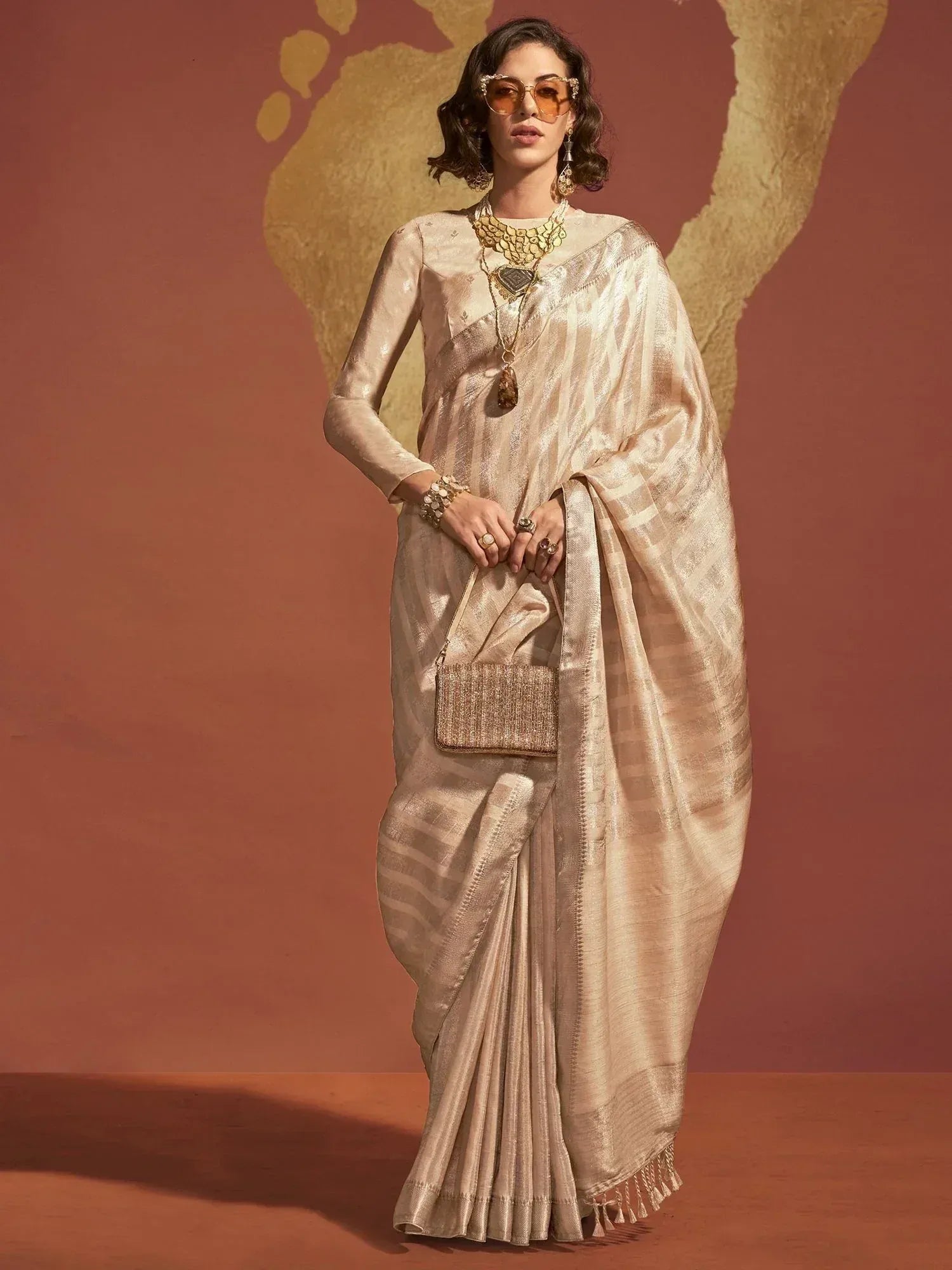 Elegant beige saree with striped pattern, paired with gold jewelry and matching clutch, perfect for Indian ethnic occasions.