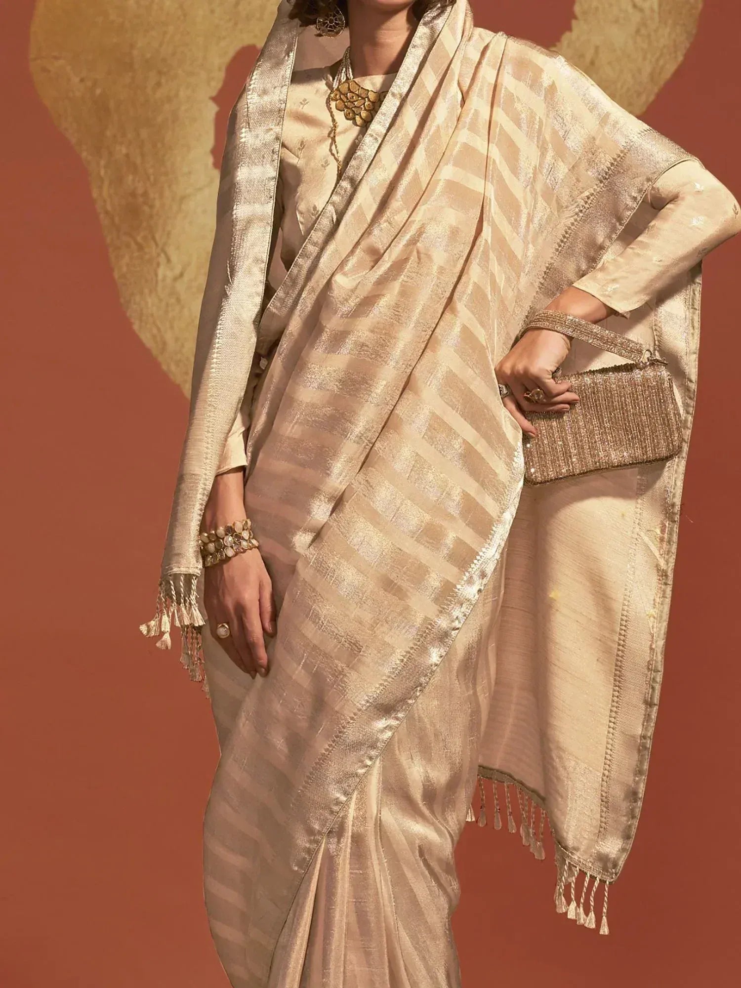Elegant beige saree with gold stripes and tassels, paired with matching blouse and jewelry for festive occasions.