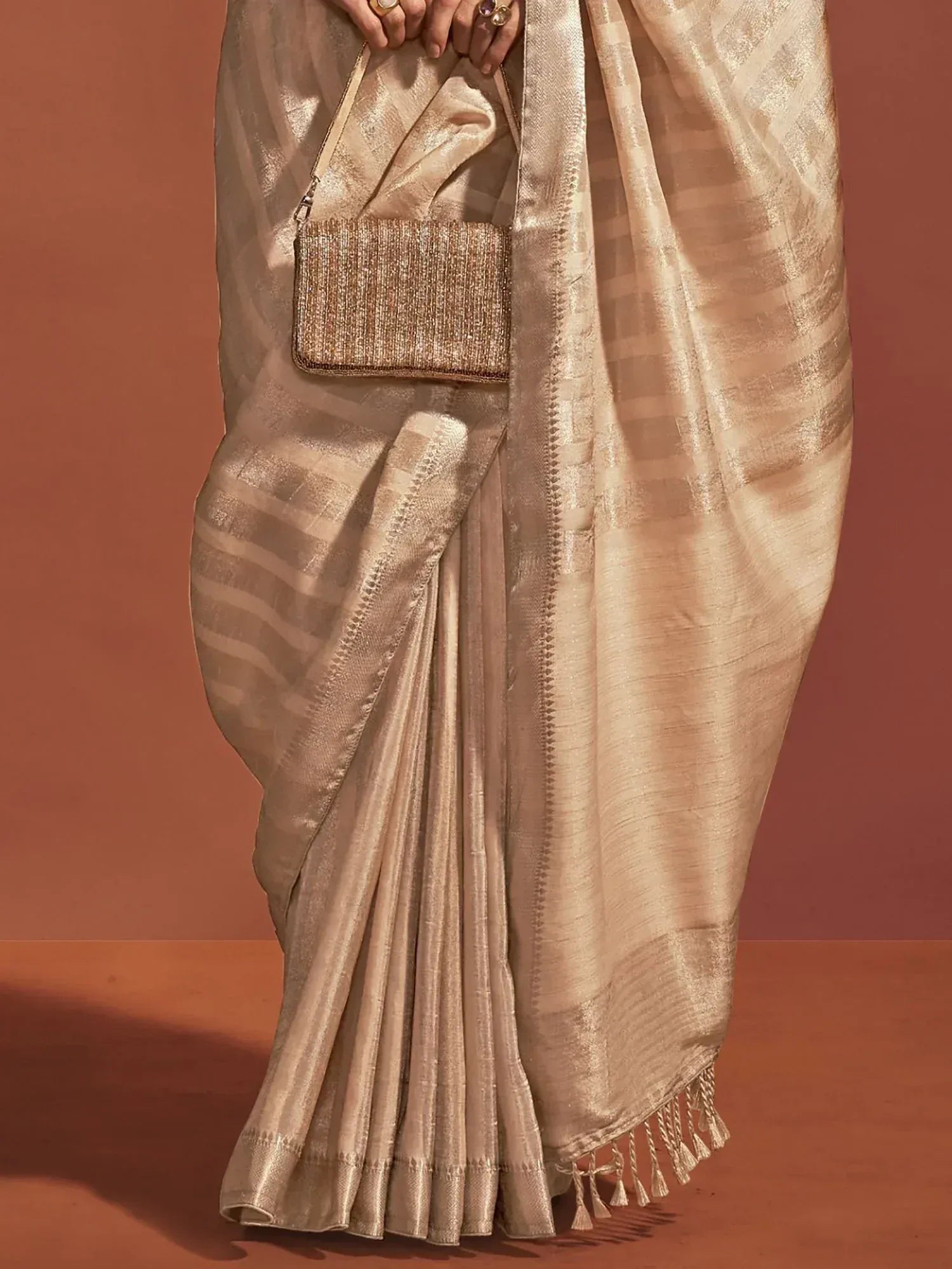 Elegant beige saree with woven checks and tassels, paired with a shimmering clutch for Indian ethnic wear.