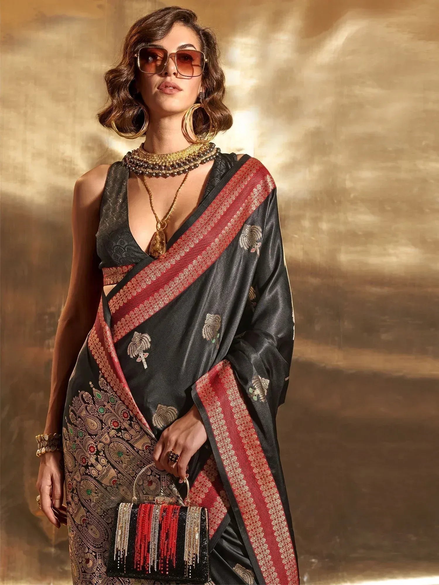 Black and red designer saree with gold embroidery, paired with statement jewelry and sunglasses