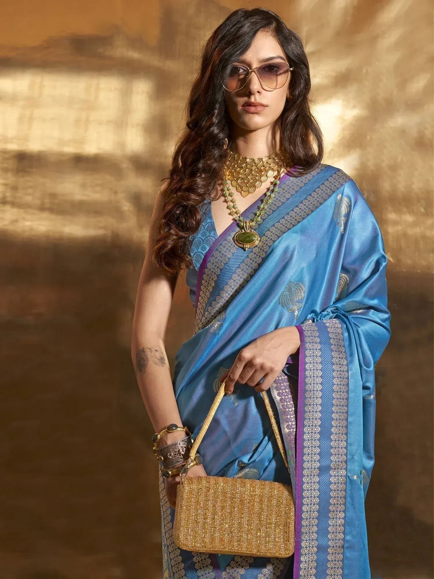 Blue silk saree with gold embroidery, ethnic jewelry, and golden handbag for Indian festive wear