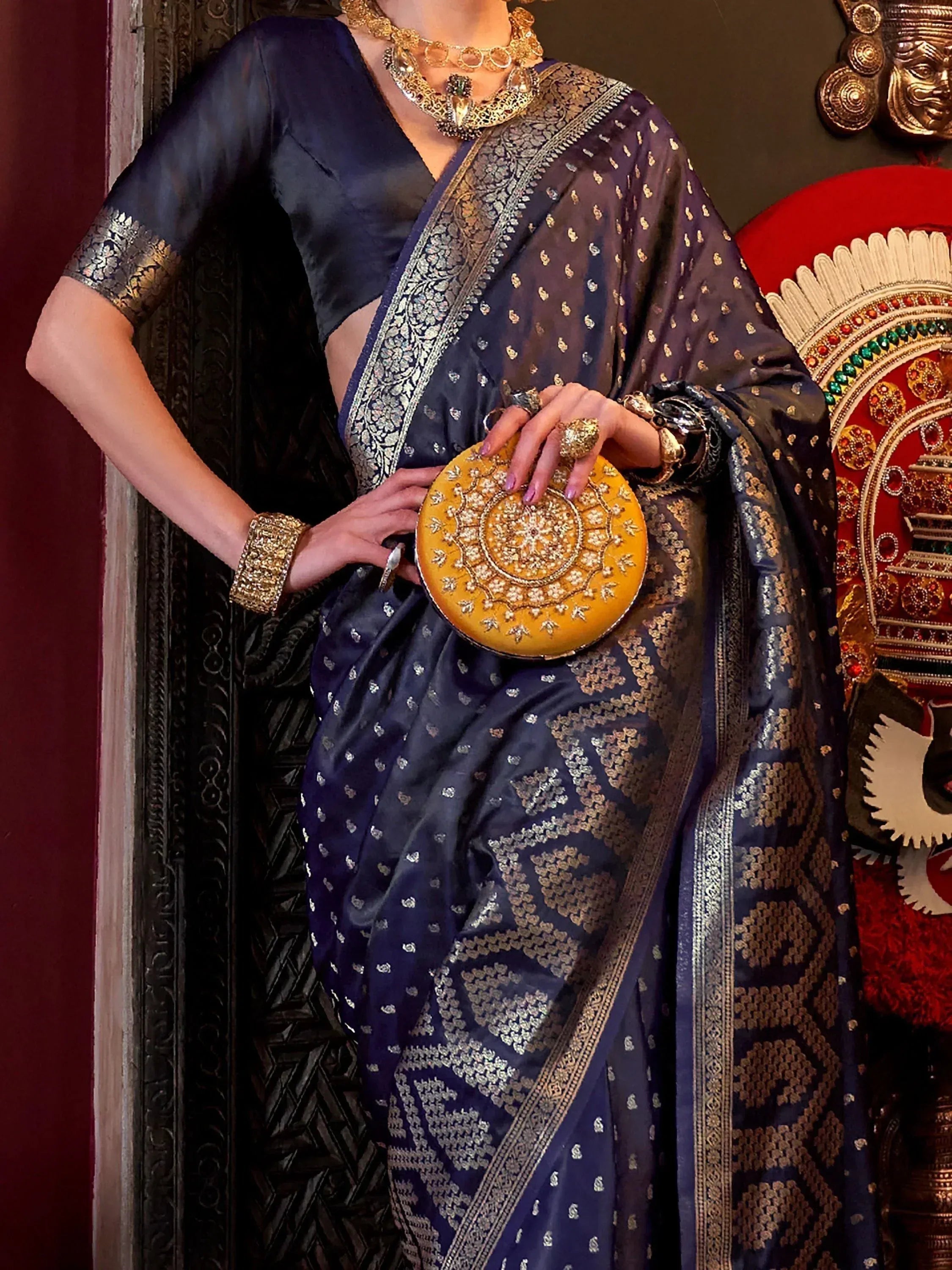 Elegant navy blue saree with gold zari work, paired with traditional jewelry and a yellow clutch, perfect for Indian ethnic wear.