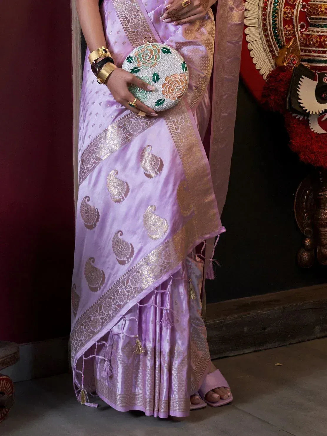 Lavender ethnic saree with gold paisley embroidery, floral clutch, and traditional jewelry
