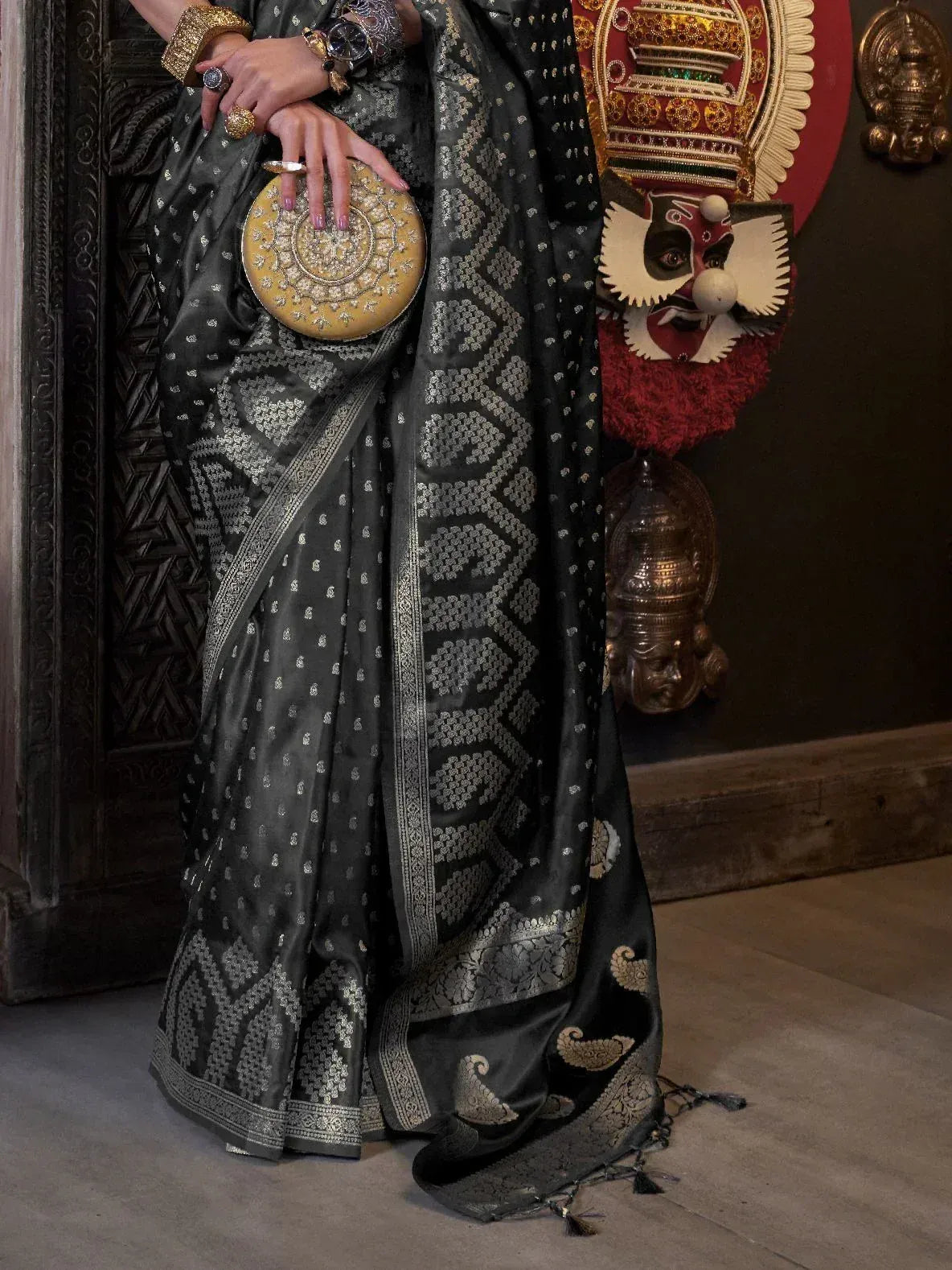 Black and silver ethnic saree with intricate woven patterns, paired with gold clutch and traditional decor