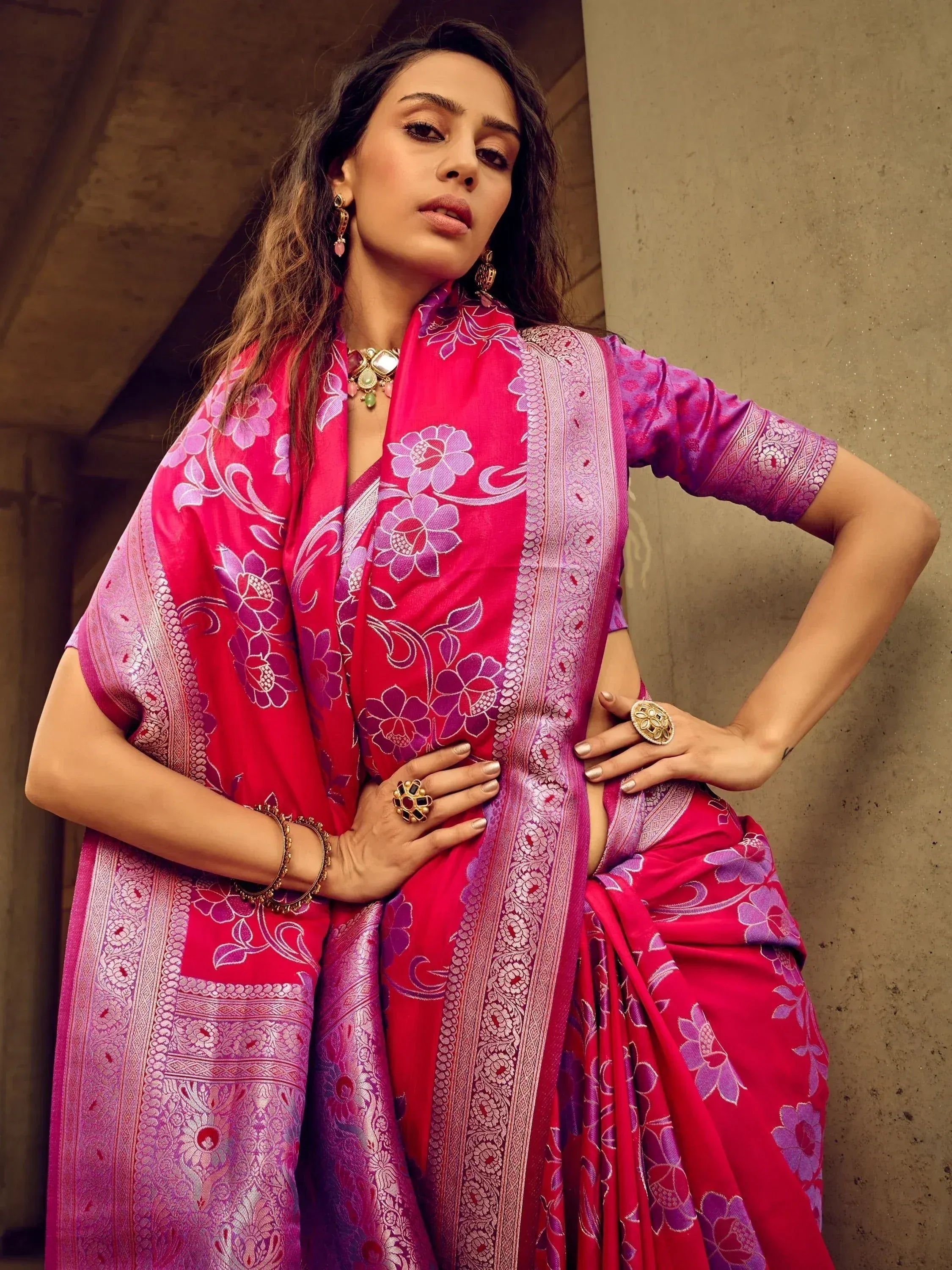 Woman in vibrant pink and purple floral saree with gold border, styled with traditional jewelry for ethnic occasions