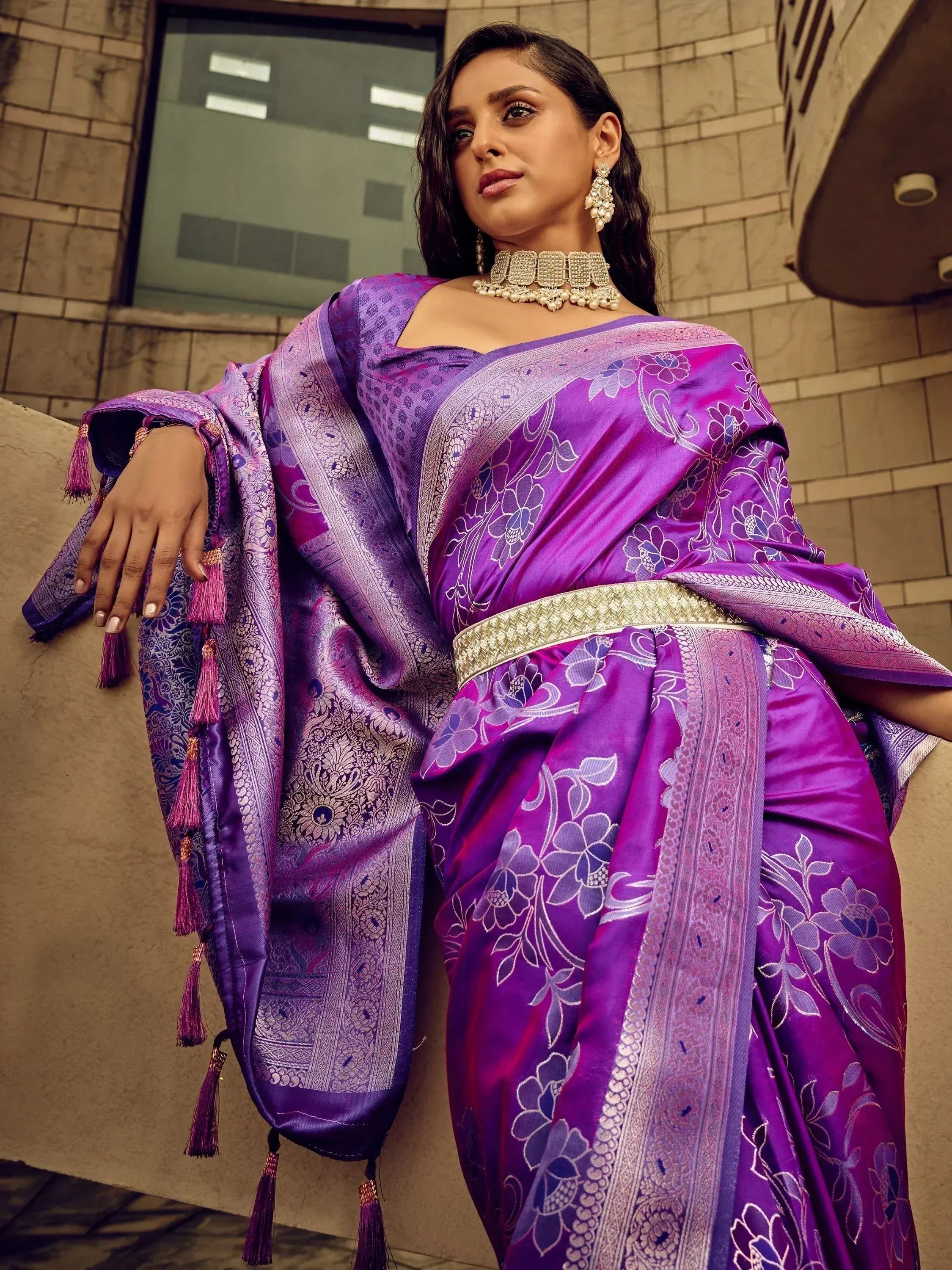 Purple floral designer saree with gold border and tassels, styled with ethnic jewelry for festive occasions