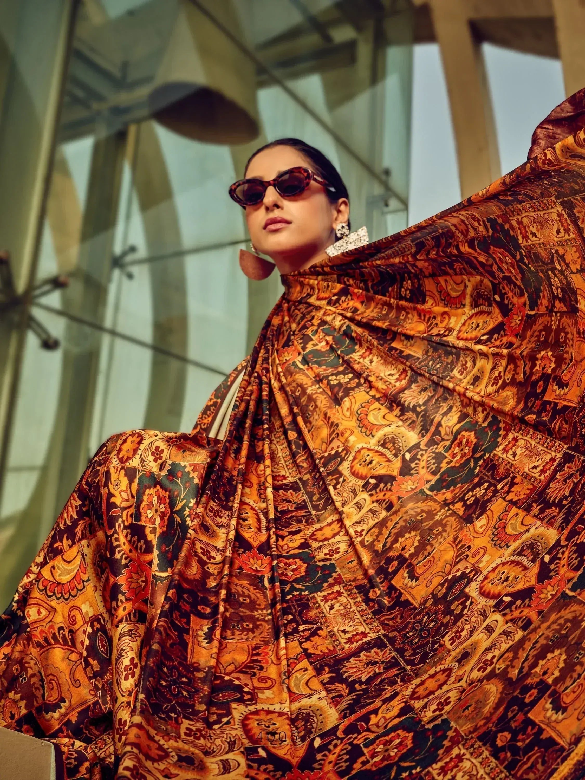Woman in vibrant ethnic printed gown with bold sunglasses, modern architectural backdrop