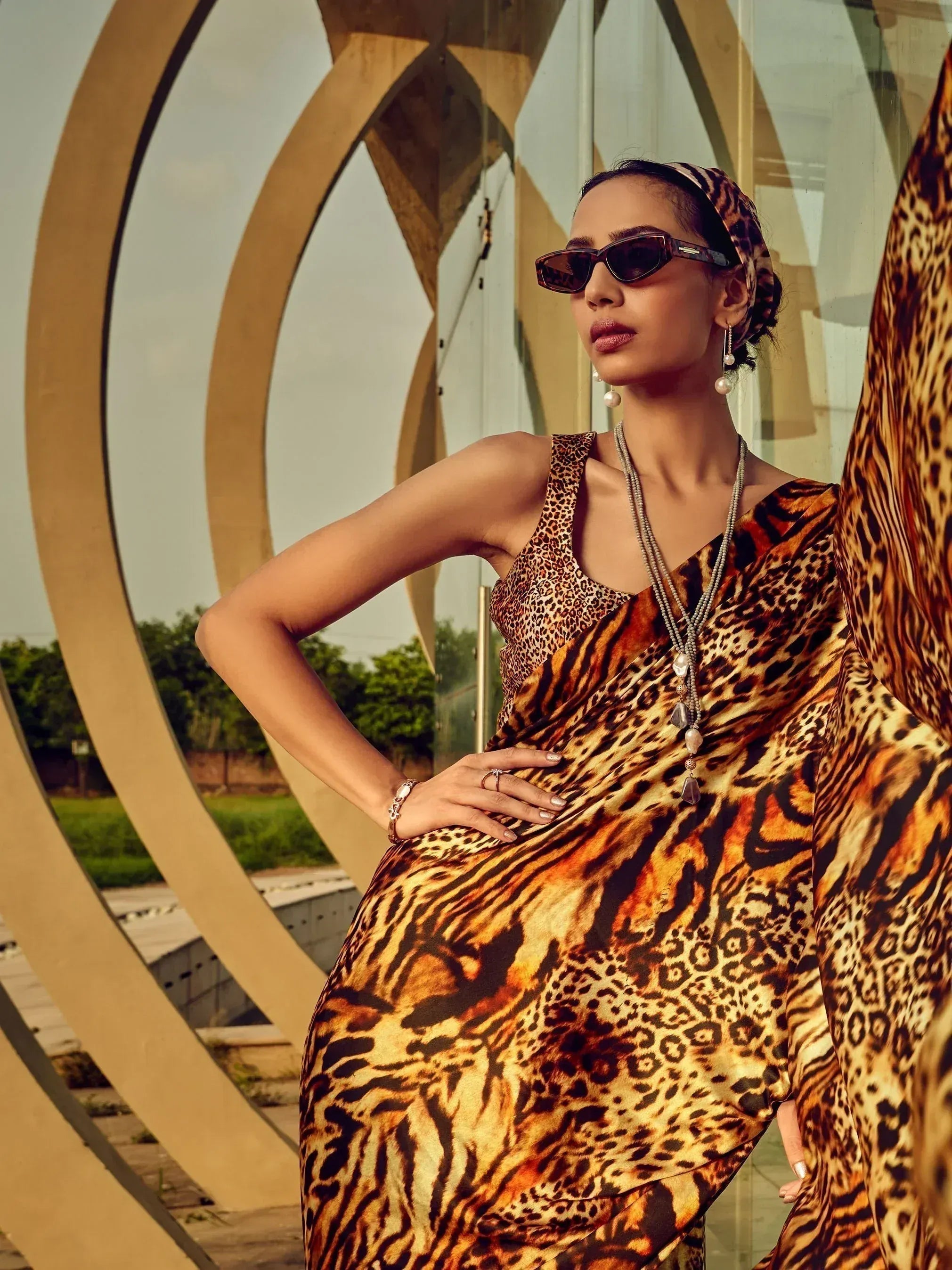 Woman in bold leopard print ethnic gown with matching headwrap, stylish sunglasses, and pearl jewelry