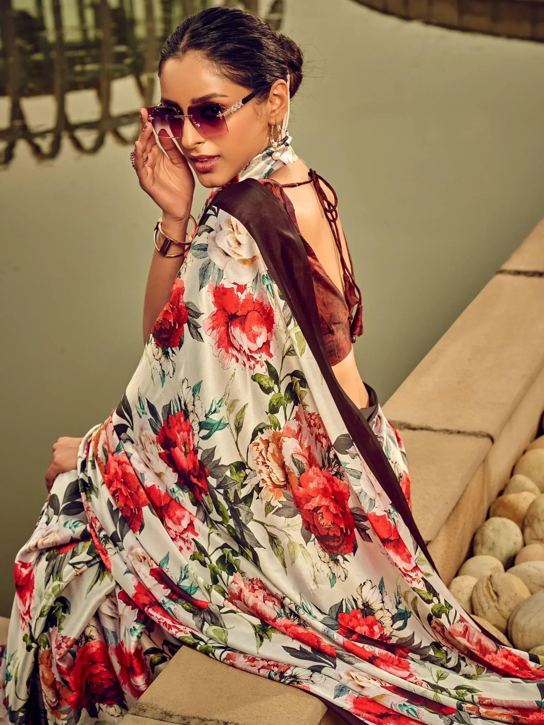 Woman in floral print saree with backless blouse, stylish sunglasses, and ethnic jewelry