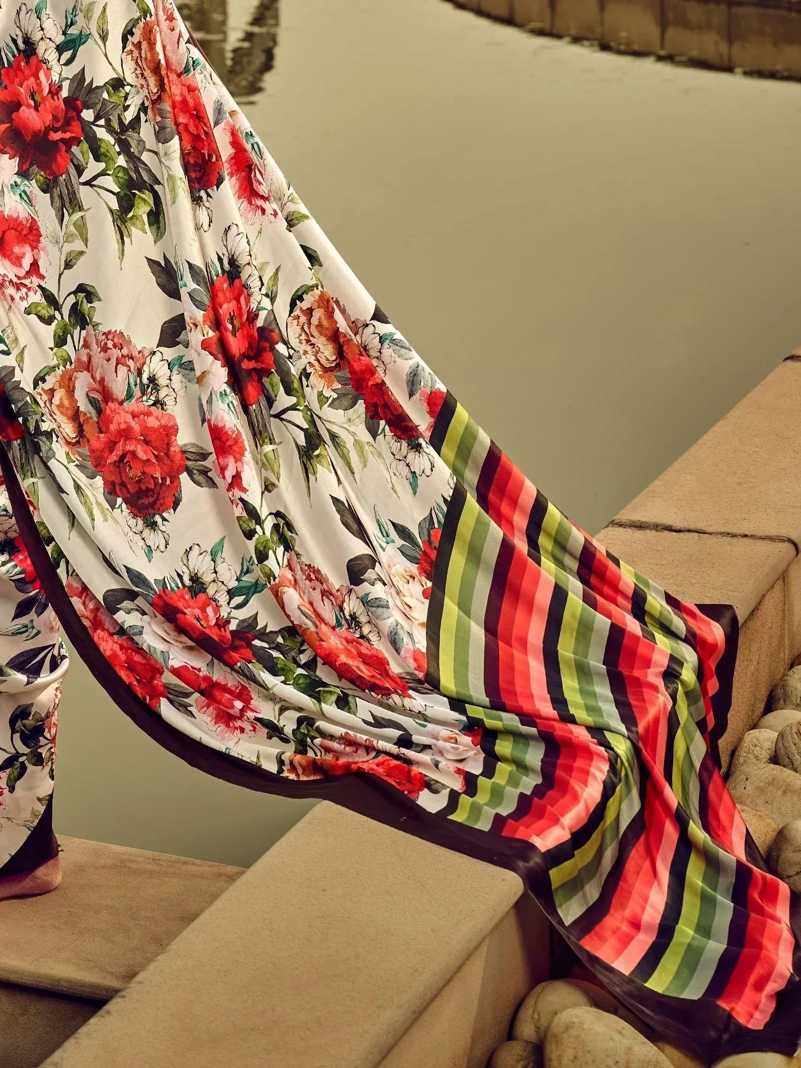 Floral print ethnic saree with vibrant red flowers and striped border, draped elegantly by water