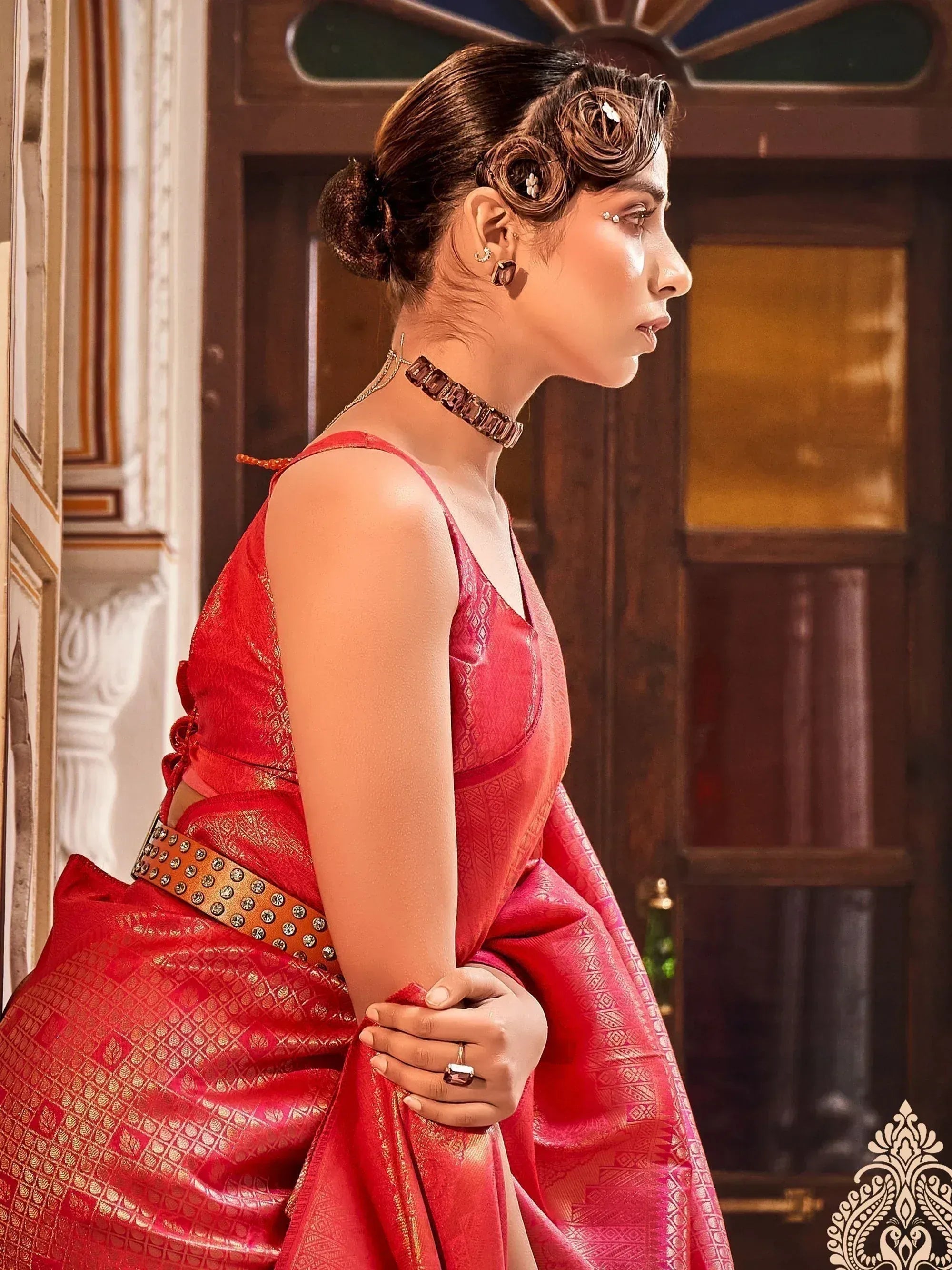 Woman in red designer saree with gold patterns, ethnic jewelry, and elegant updo hairstyle