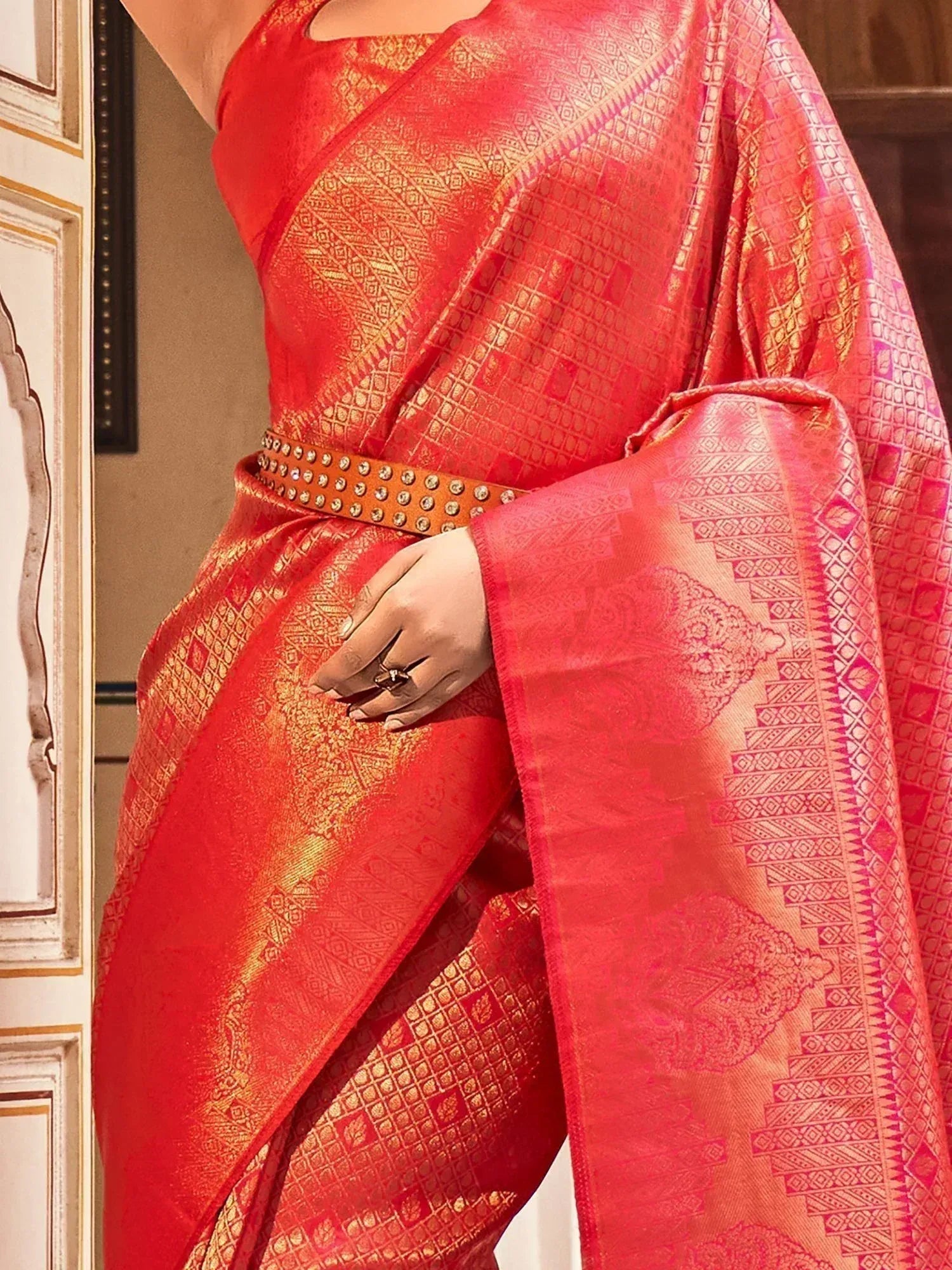 Red and gold designer saree with intricate geometric patterns and embellished belt for ethnic wear