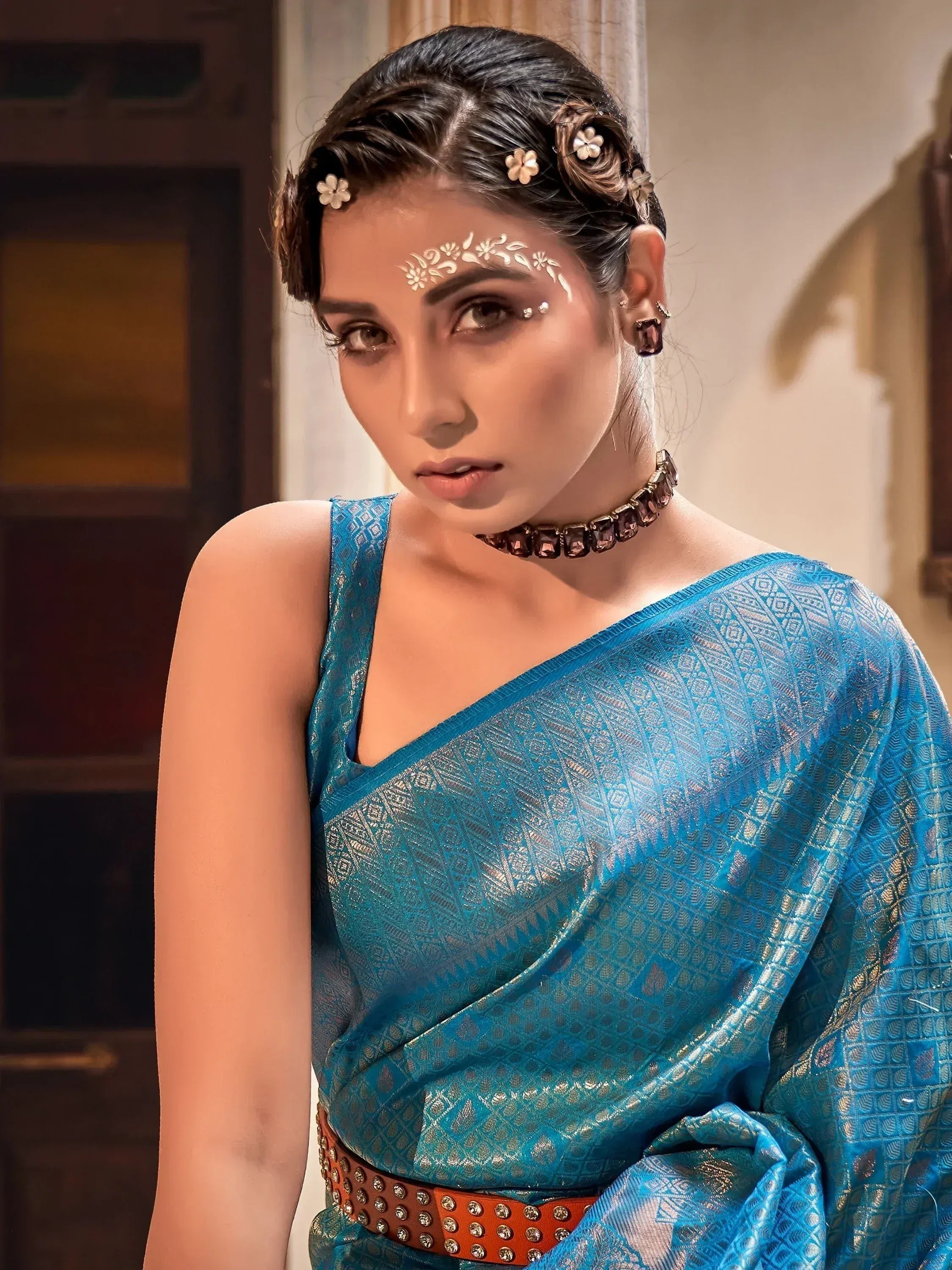 Woman in blue designer saree with gold pattern, floral hair accessories, and traditional makeup for ethnic wear