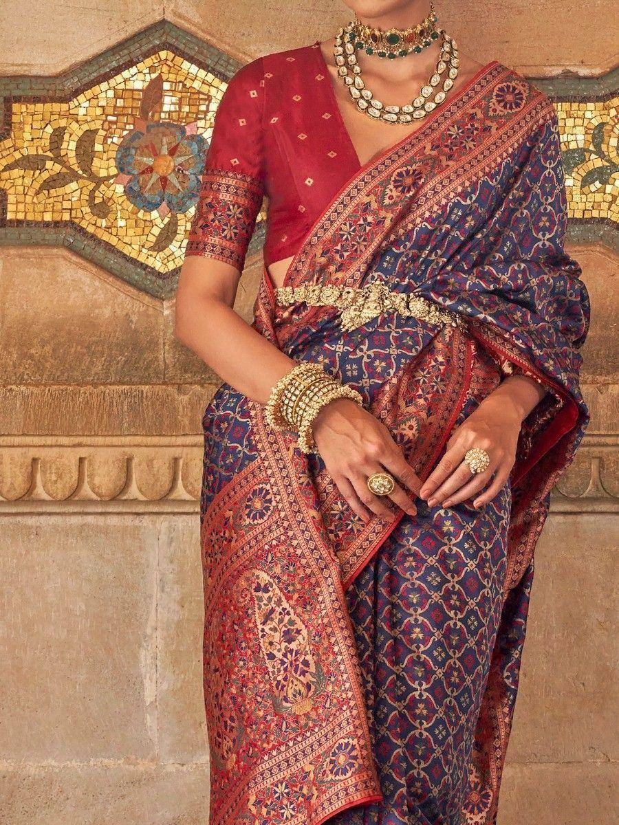 Elegant Indian saree with intricate blue and red patterns, paired with gold jewelry and a red blouse.