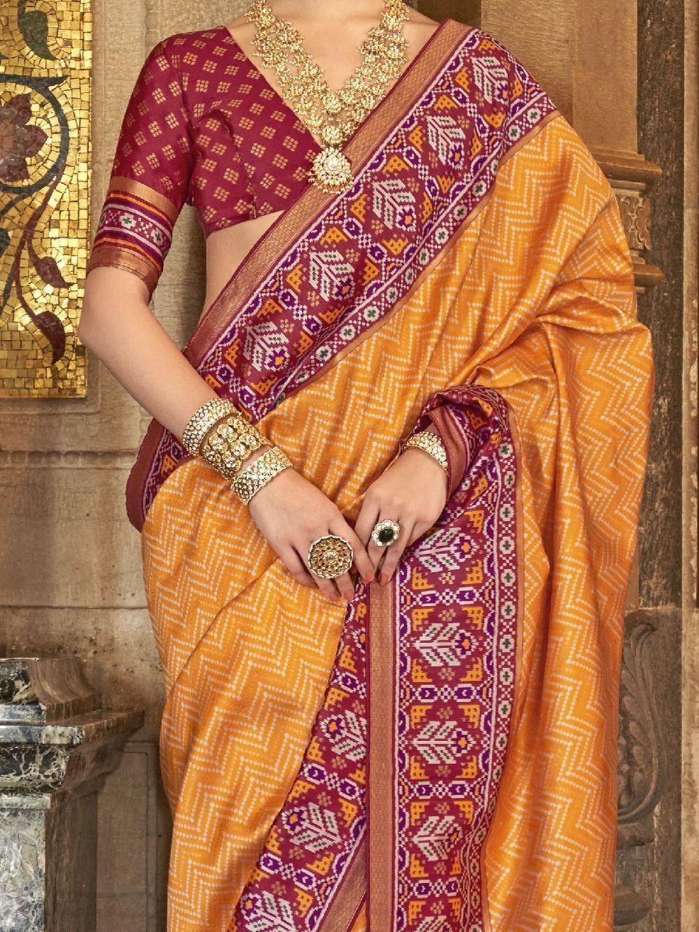 Orange and maroon ethnic saree with geometric border, paired with designer blouse and gold jewelry