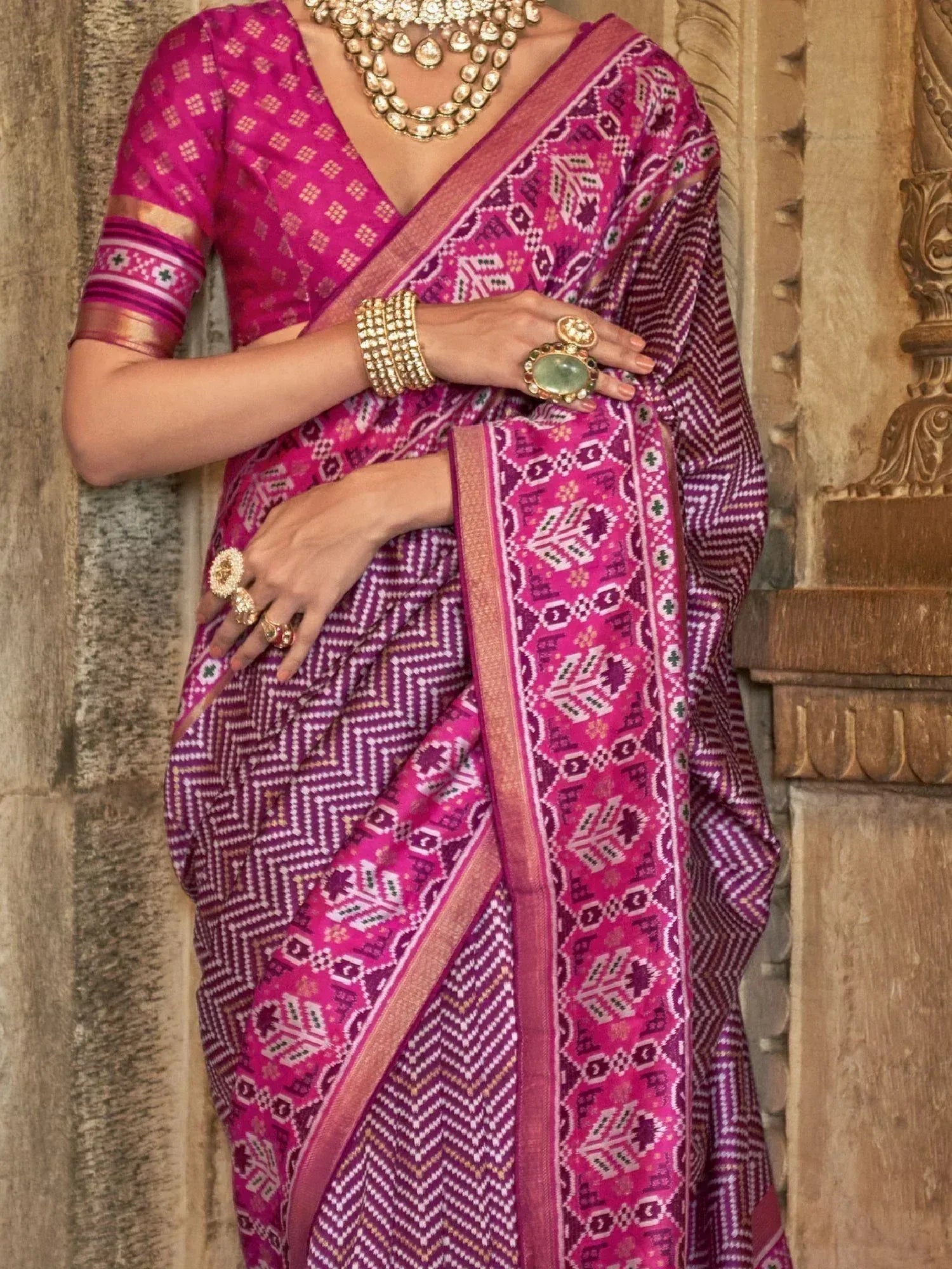 Vibrant pink and purple ethnic saree with geometric patterns, paired with traditional gold jewelry for festive occasions.