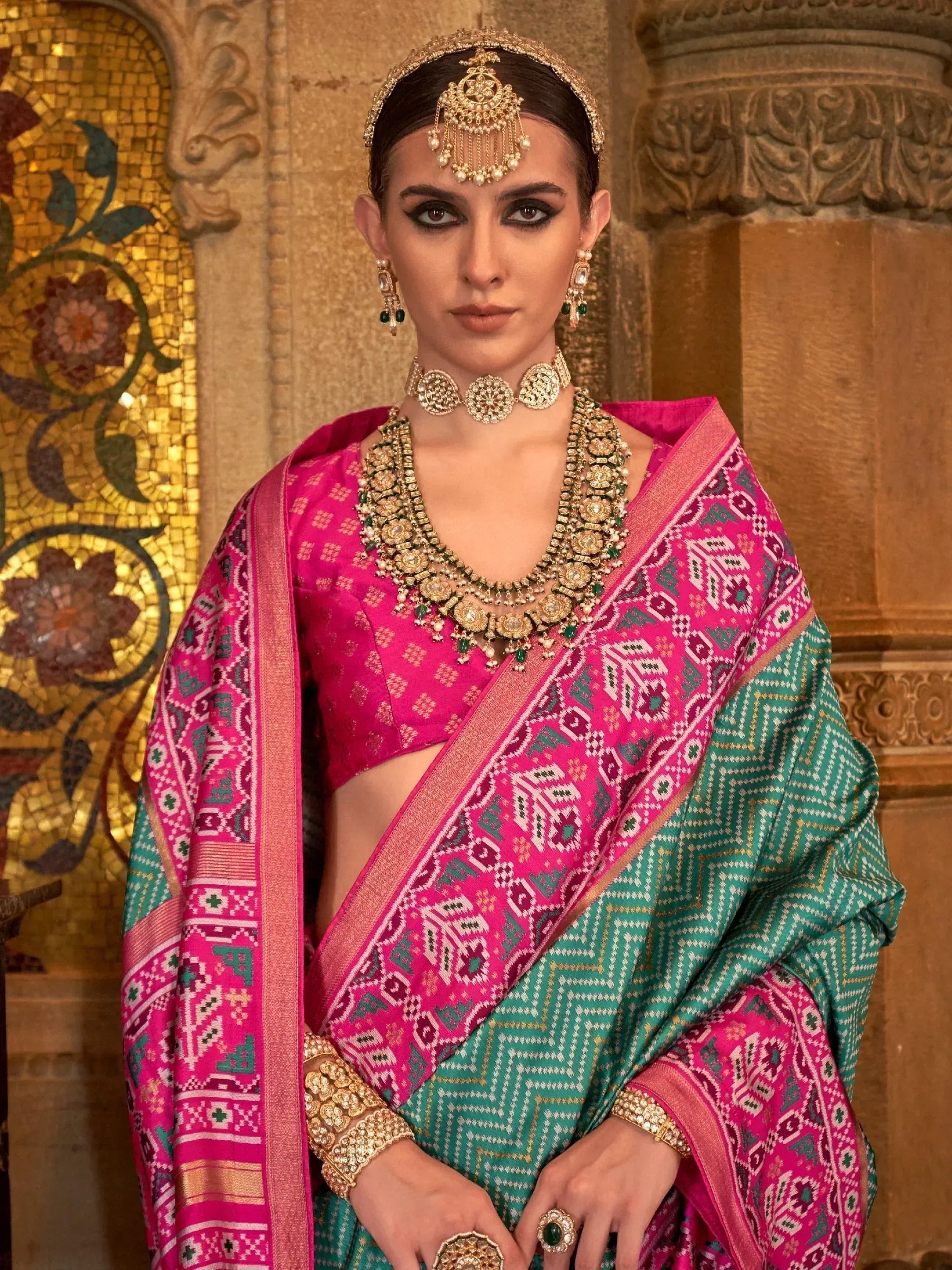 Woman in vibrant pink and green ethnic saree with intricate patterns and traditional gold jewelry