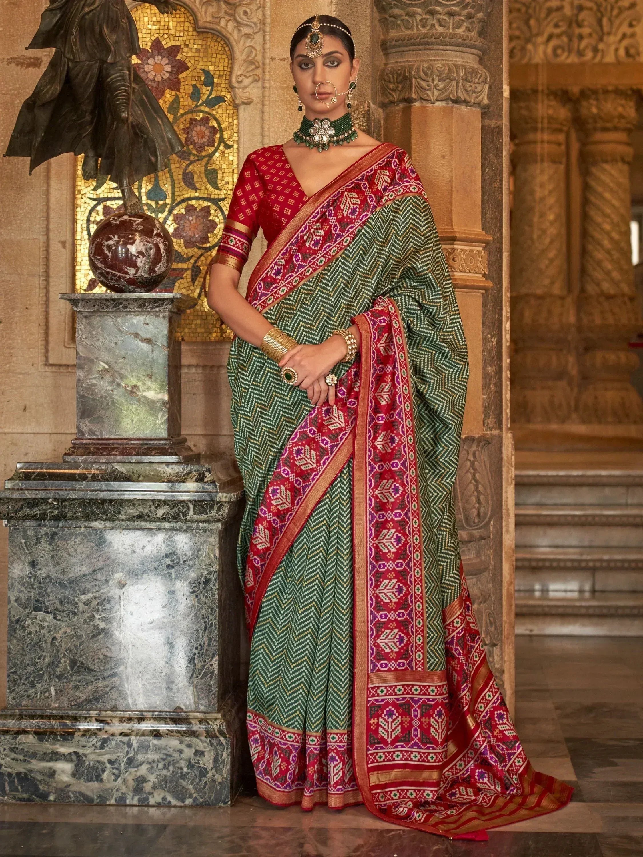 Woman in green and red ethnic saree with intricate patterns, traditional jewelry, and temple backdrop