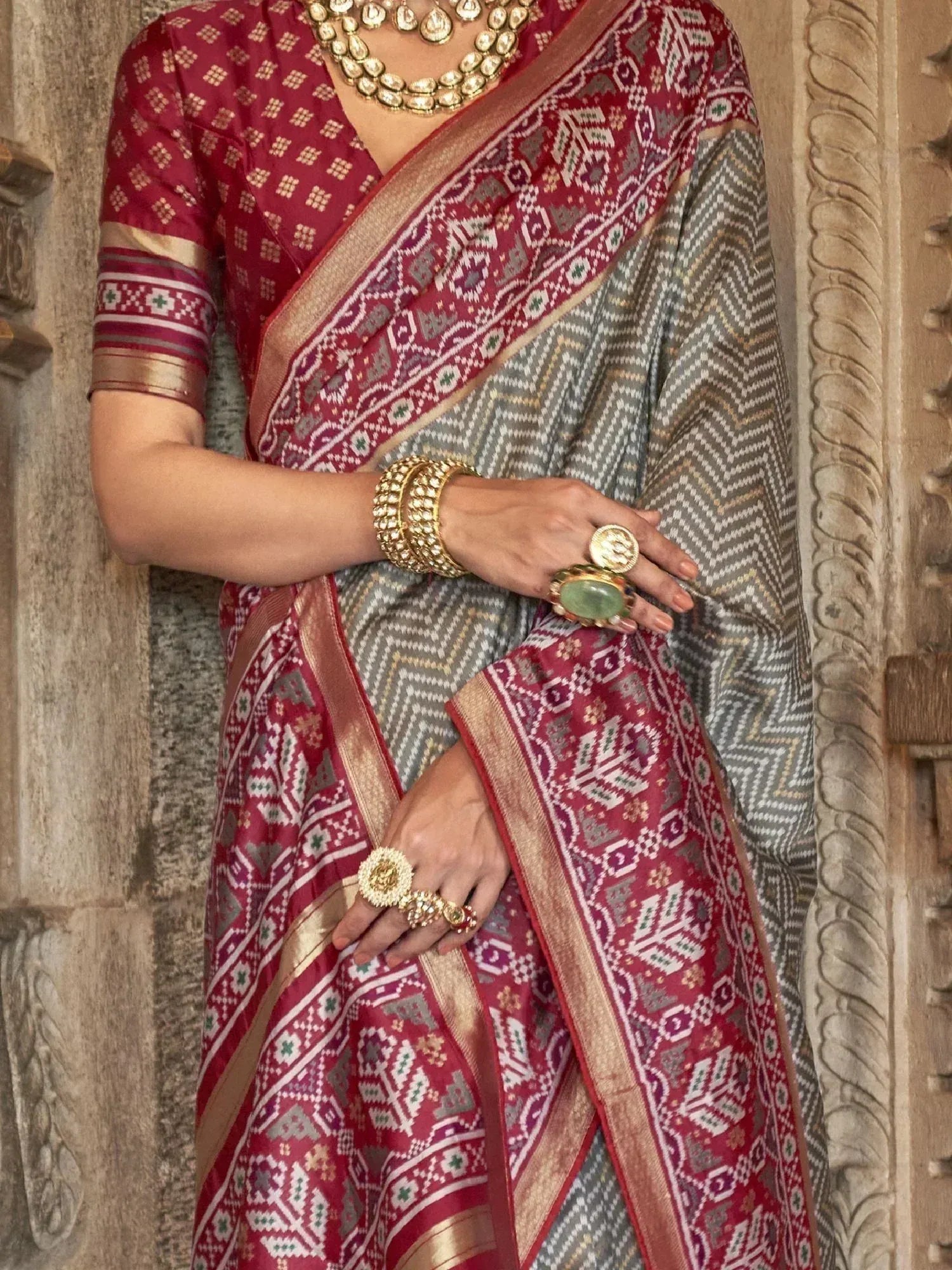 Red and grey ethnic saree with intricate geometric patterns, gold border, and traditional jewelry