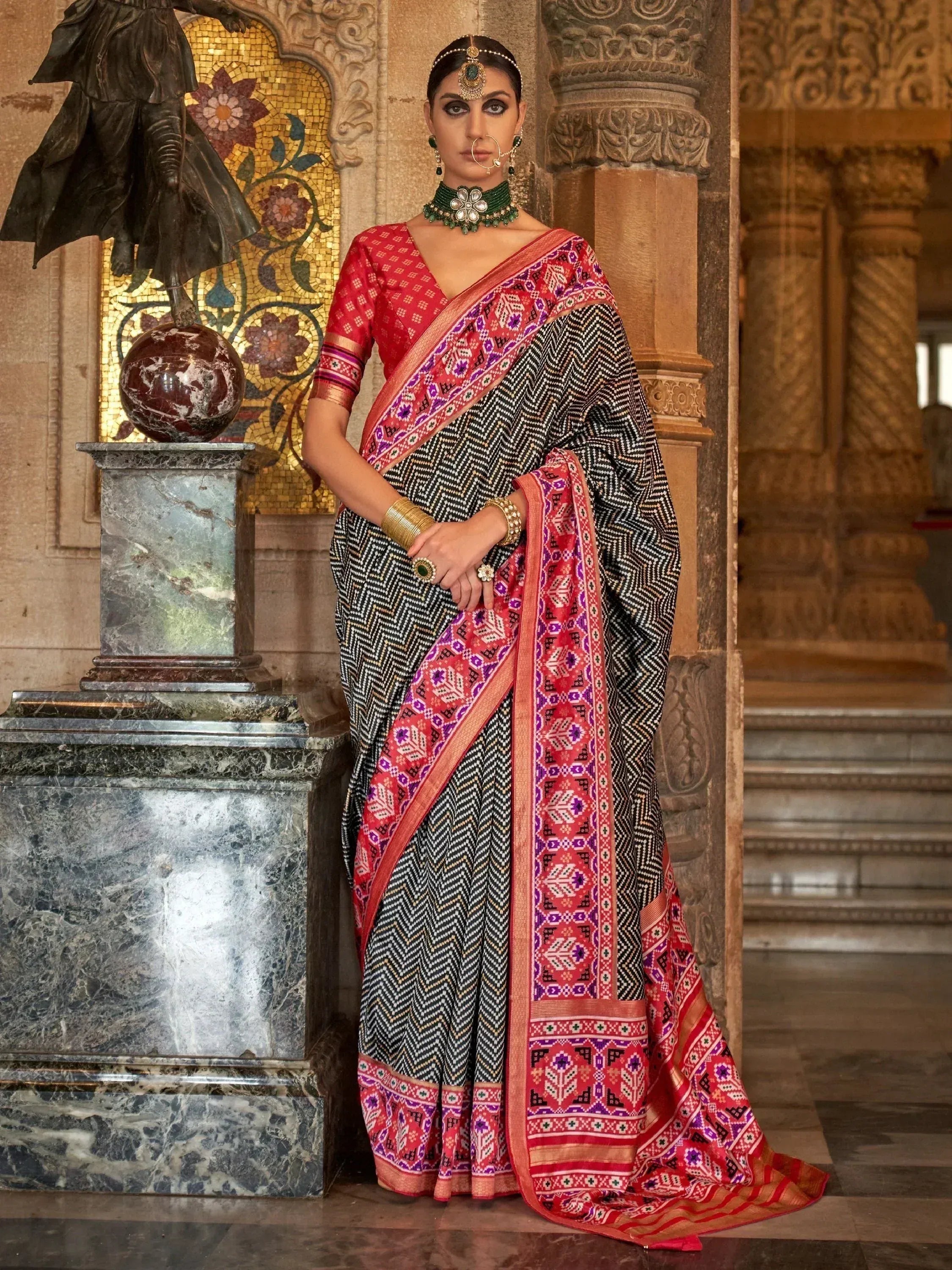 Woman in black and red ethnic saree with geometric print, traditional jewelry, palace backdrop