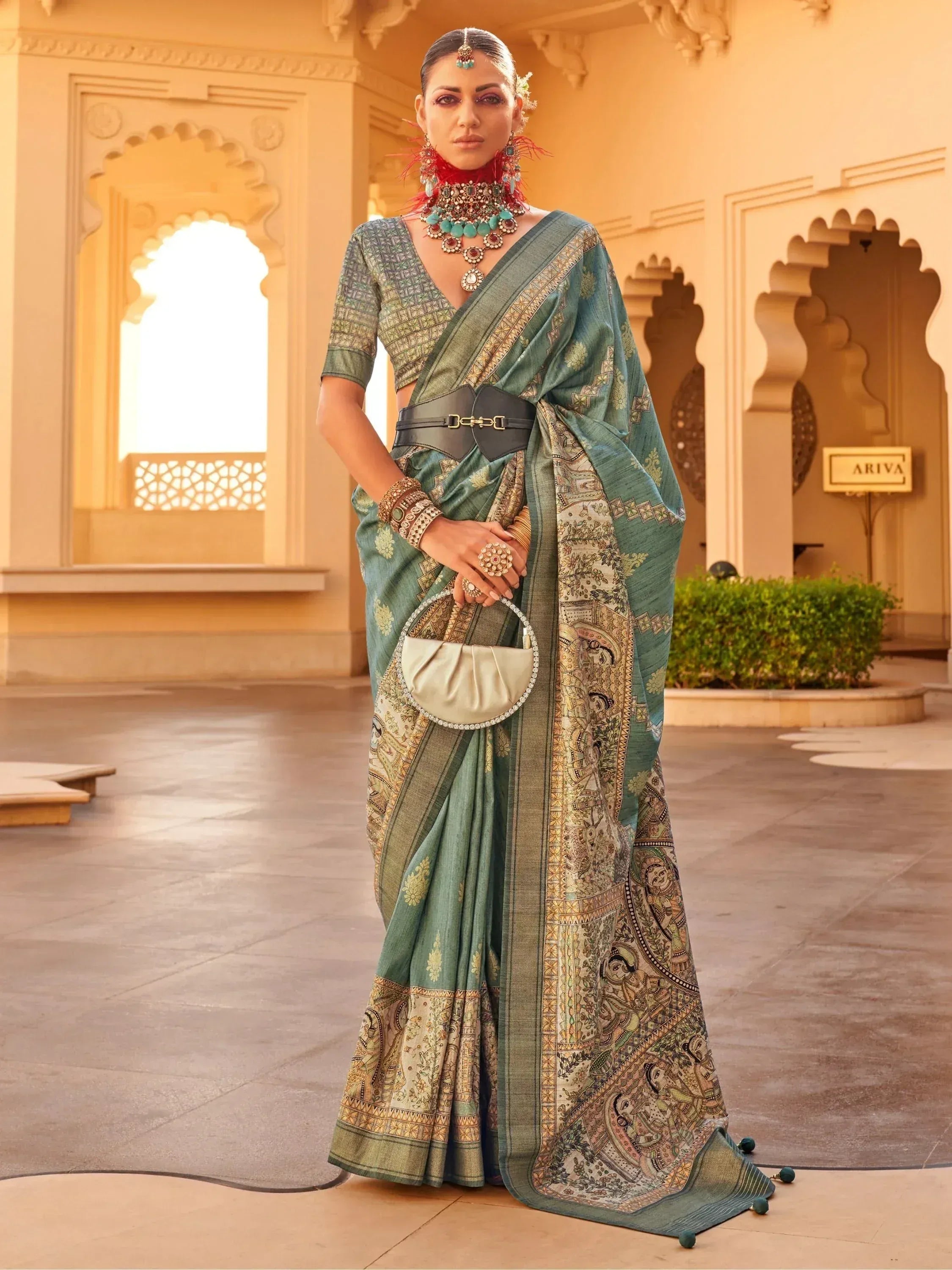 Elegant teal saree with intricate paisley print, paired with statement jewelry and a modern belt for ethnic wear.