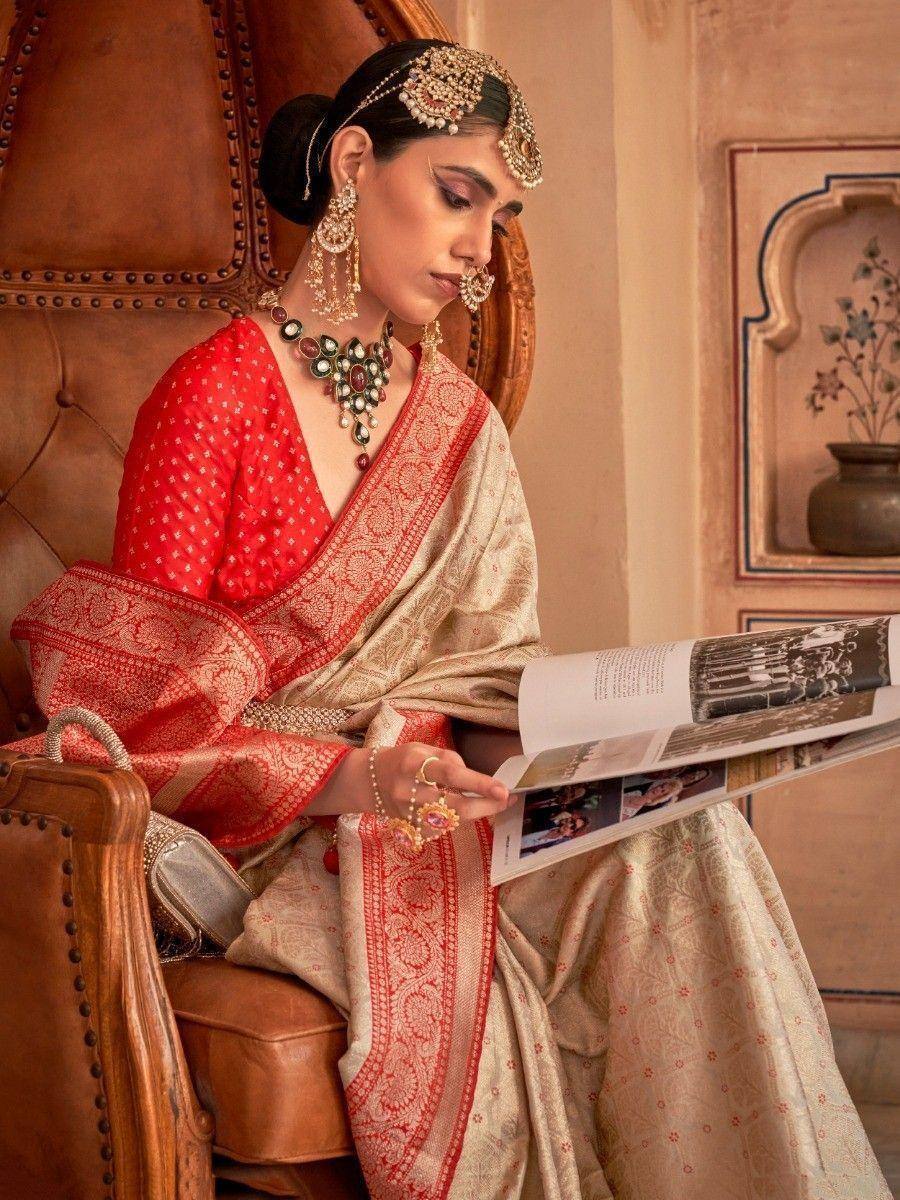 Elegant woman in red and gold Indian saree with traditional jewelry, seated reading magazine