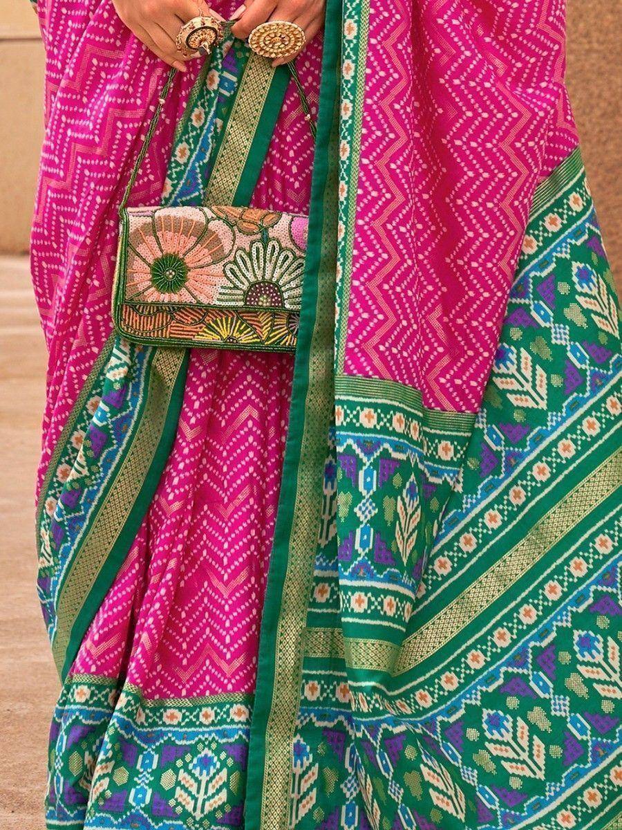 Vibrant pink and green ethnic saree with intricate geometric patterns and floral embroidered clutch