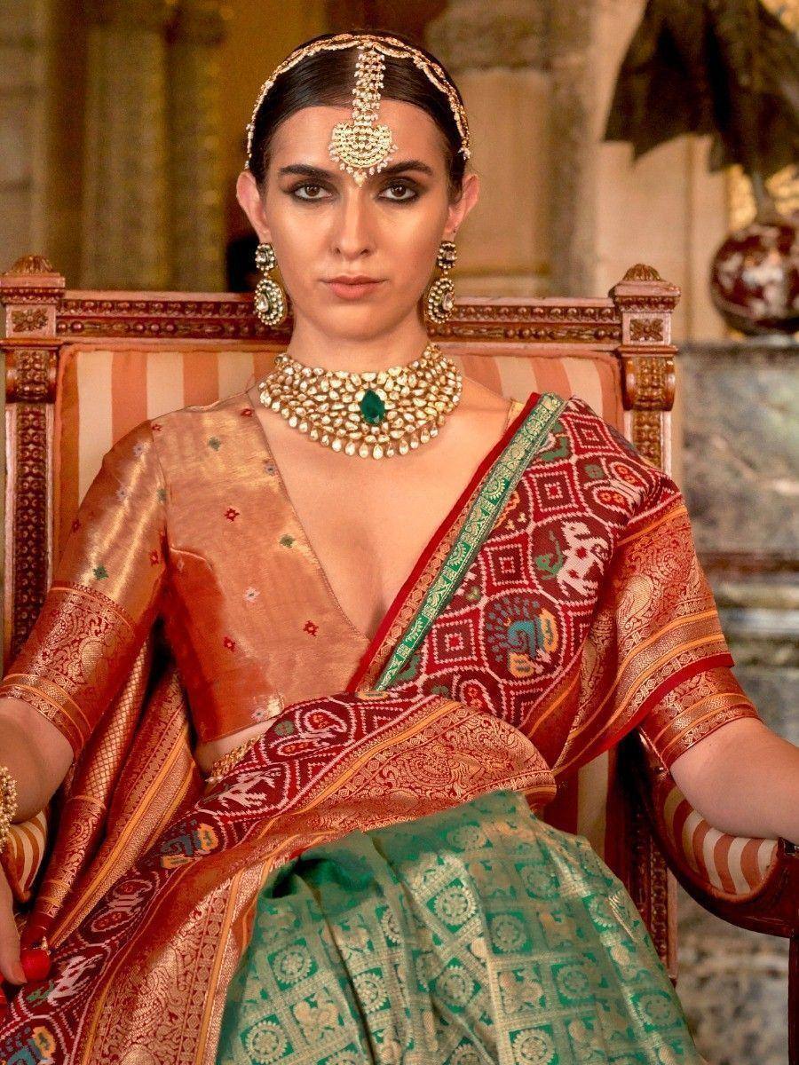 Woman in traditional Indian saree with intricate embroidery and gold jewelry, seated on ornate chair