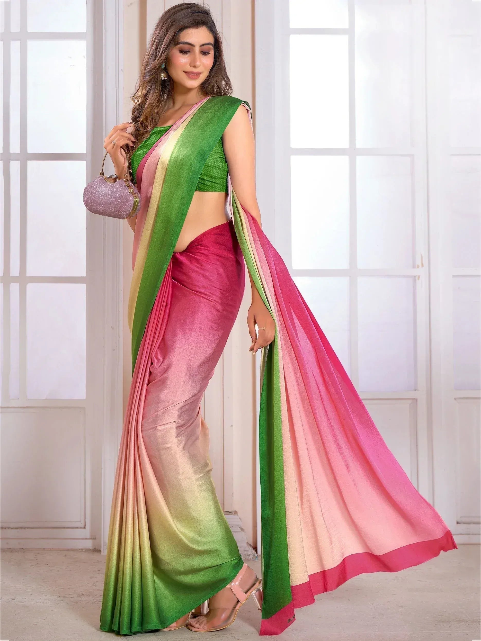 Woman in vibrant ombre saree with green, pink, and gold hues, paired with matching blouse and clutch, ideal for ethnic occasions.