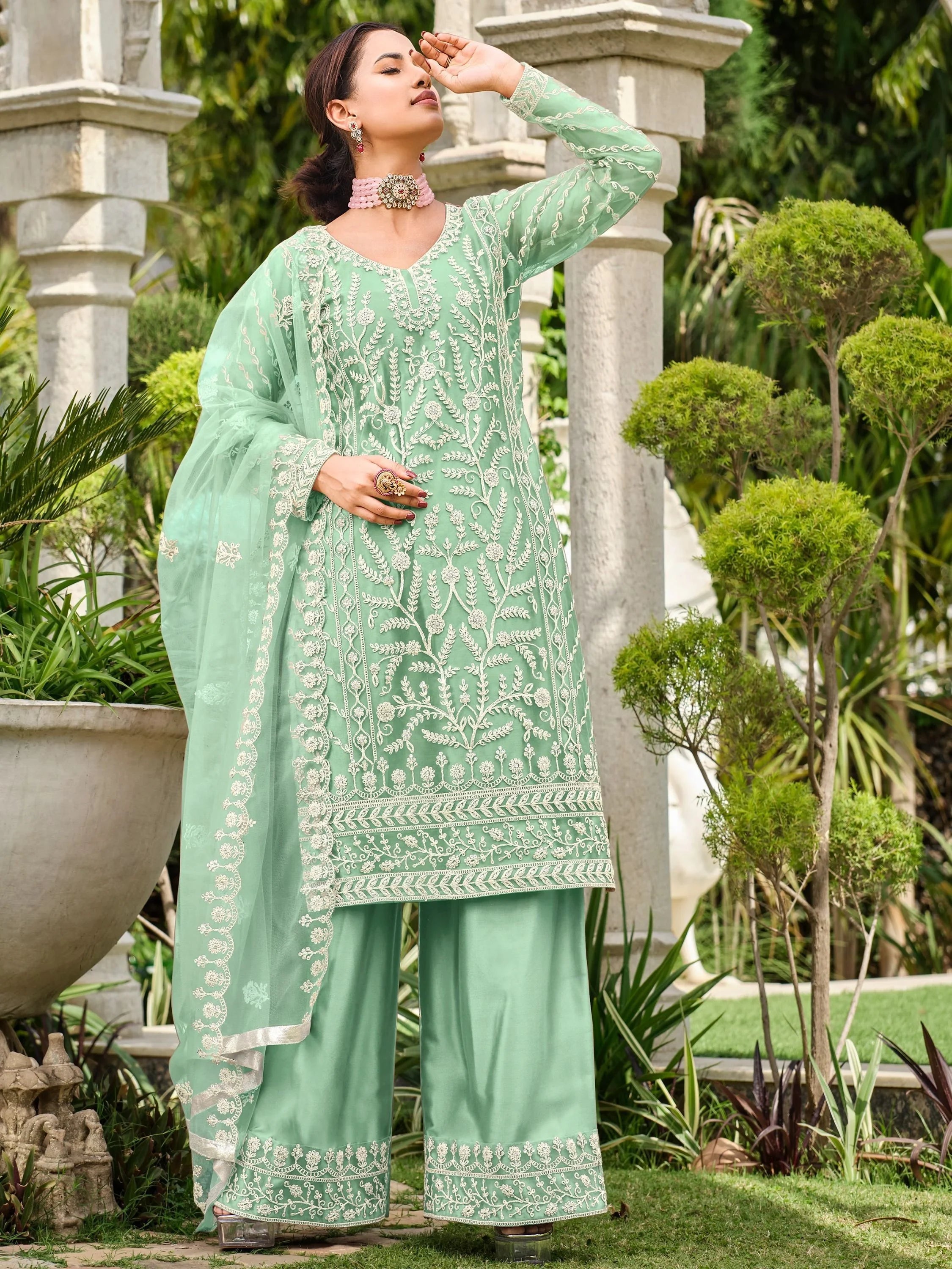 Woman wearing pastel green embroidered salwar kameez with dupatta in garden setting