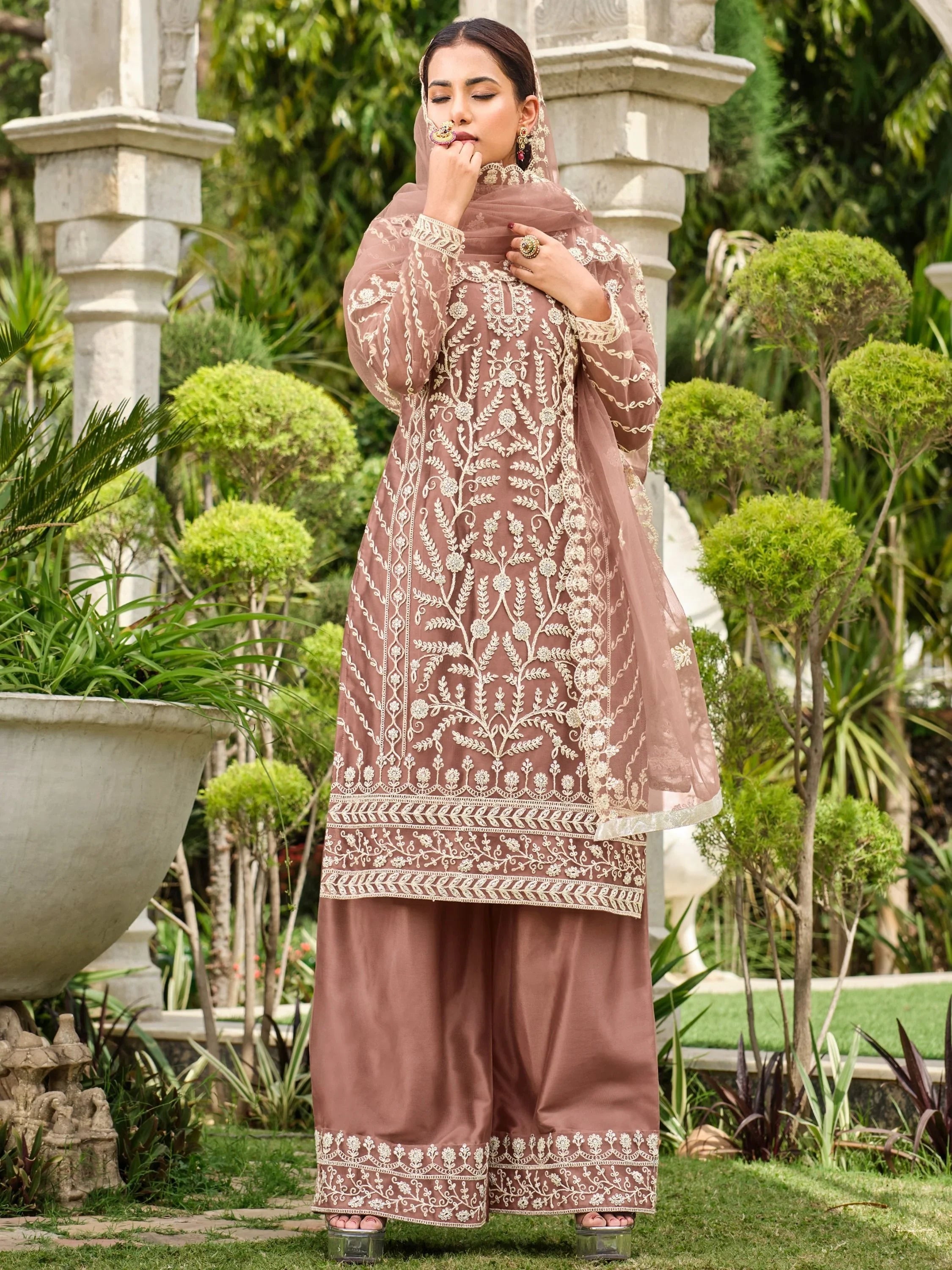 Woman wearing brown embroidered salwar kameez with dupatta in garden setting