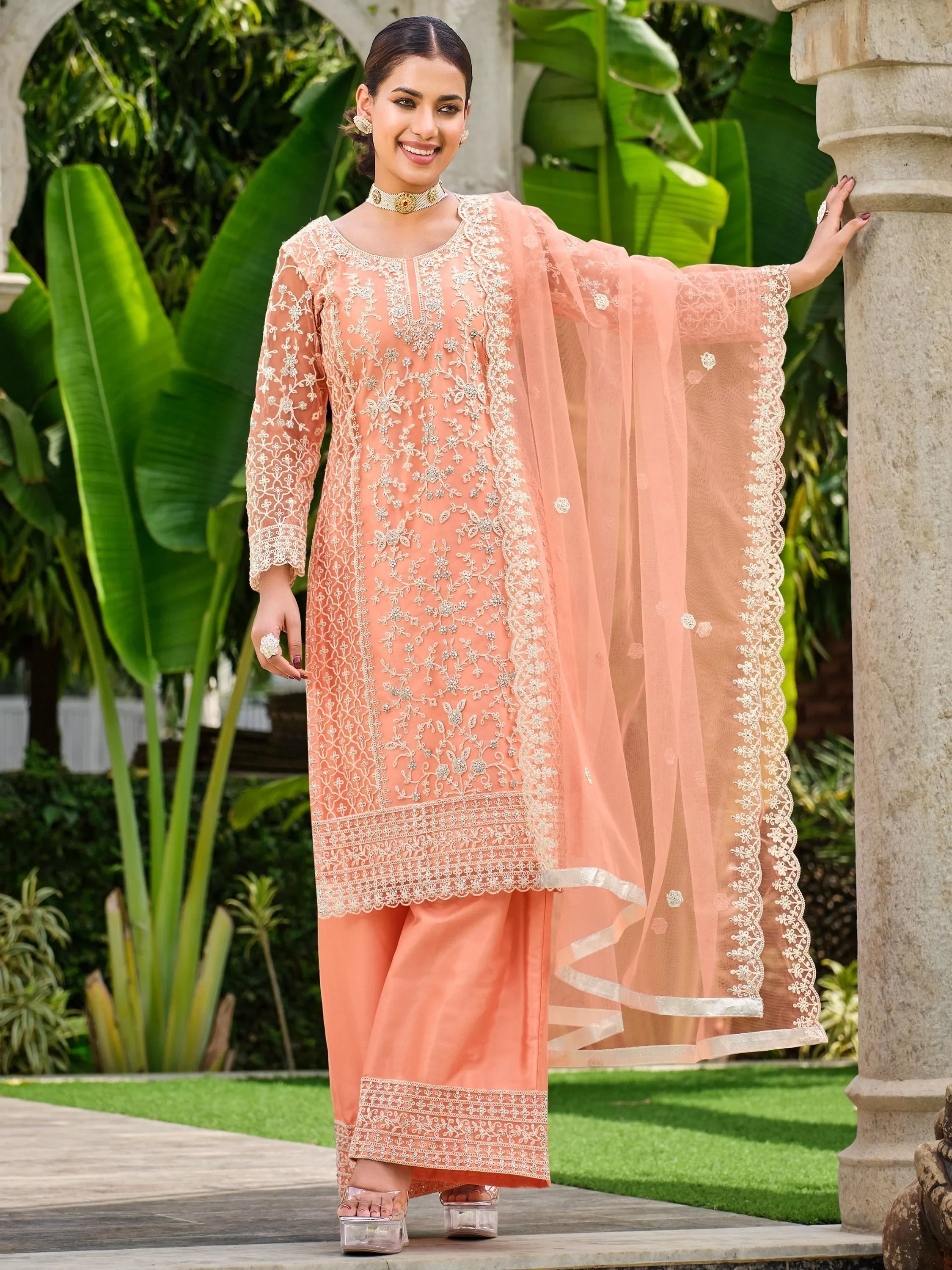 Woman wearing peach embroidered salwar kameez with dupatta, standing outdoors