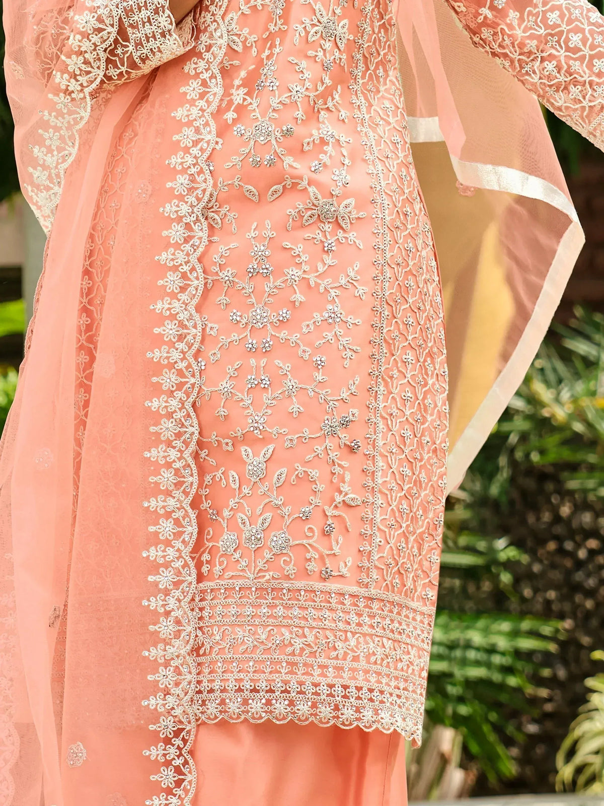 Peach ethnic gown with intricate white floral embroidery and sheer sleeves, perfect for Indian occasions.