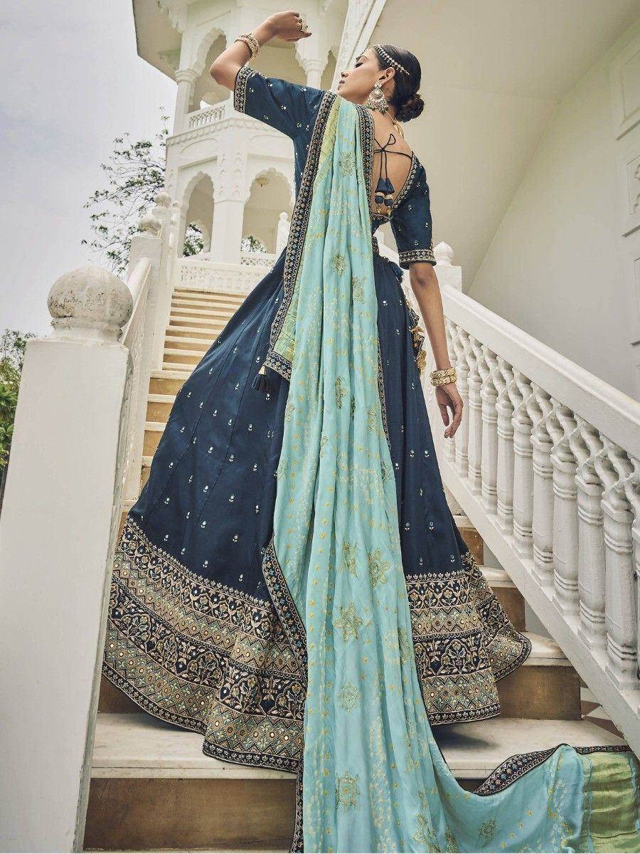 Woman in navy blue designer lehenga choli with gold embroidery, paired with light blue dupatta, standing on stairs