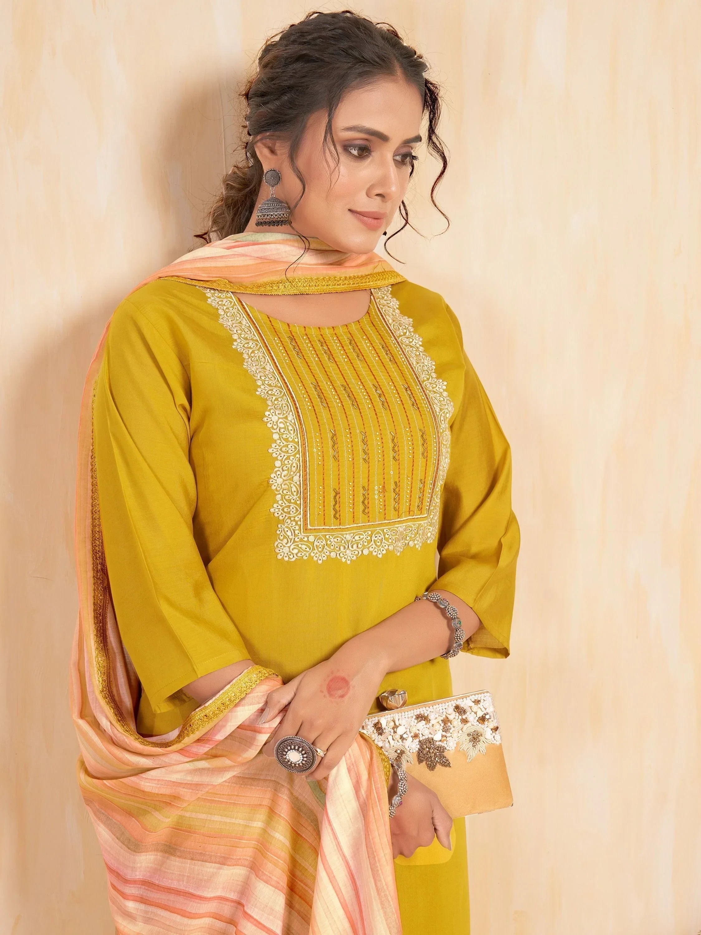 Woman in mustard yellow embroidered kurti with striped dupatta, holding embellished clutch