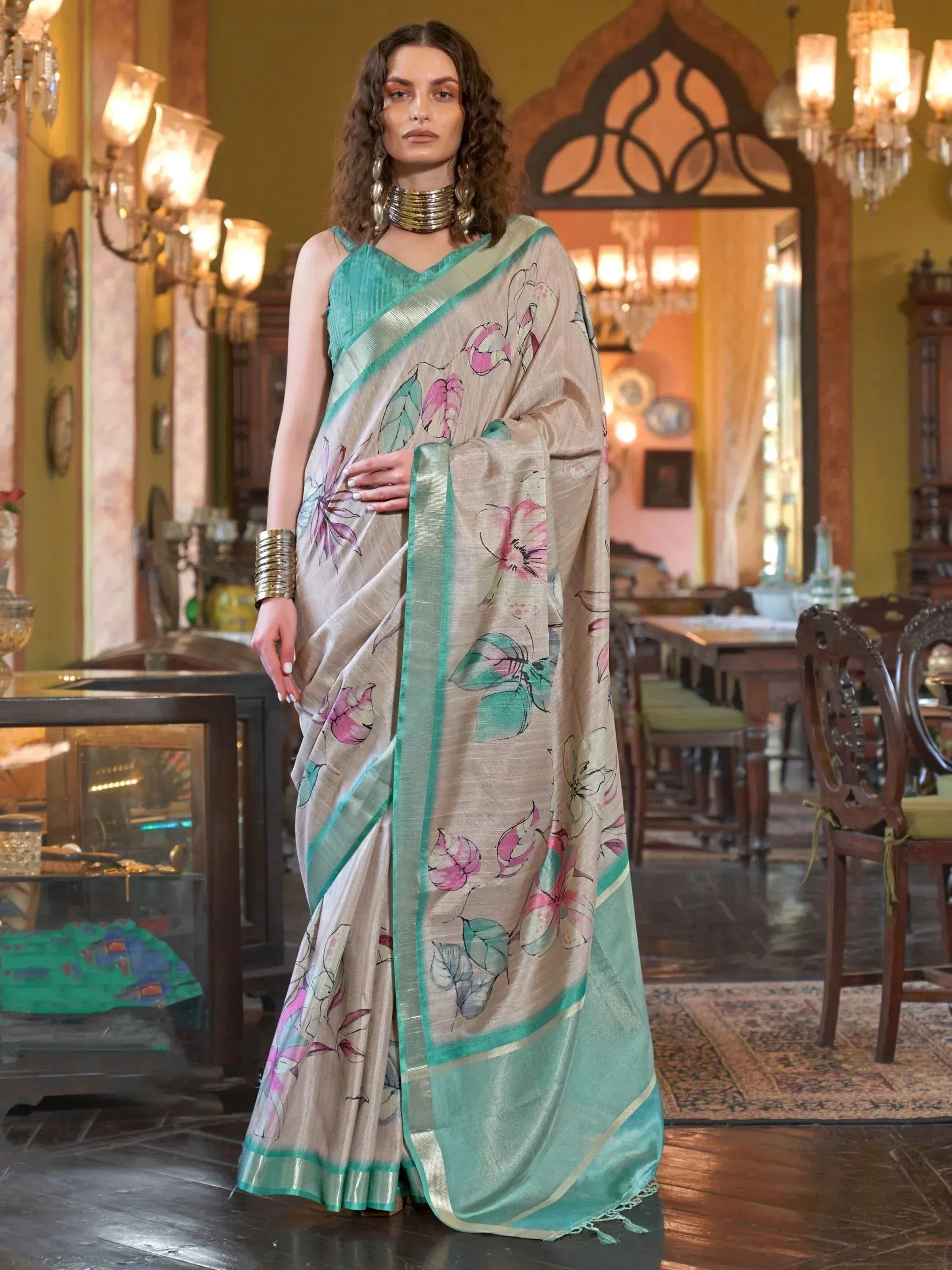 Beige floral saree with teal border, styled with ethnic jewelry in a traditional Indian setting