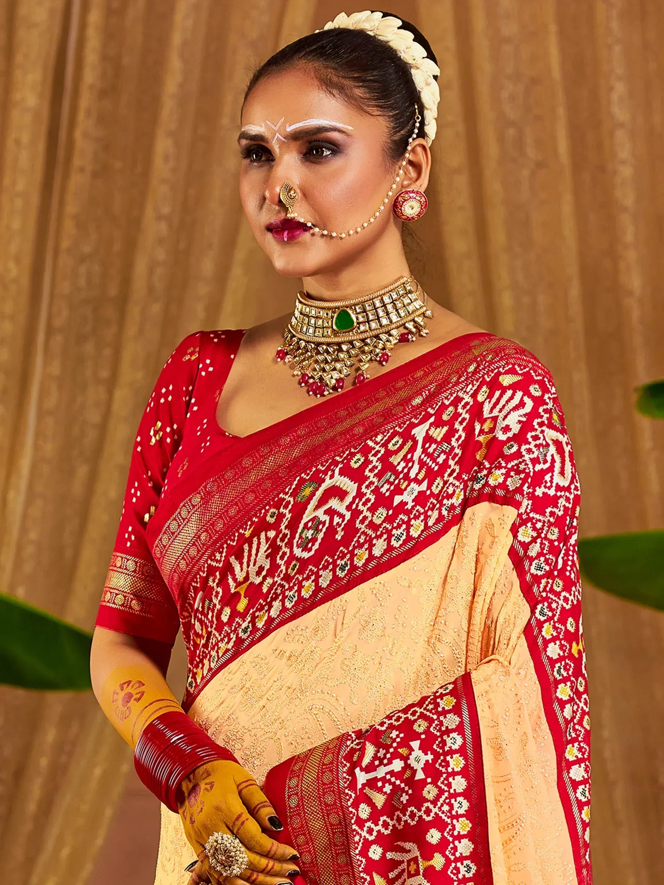 Red and beige ethnic saree with intricate embroidery, traditional jewelry, and floral hair accessory