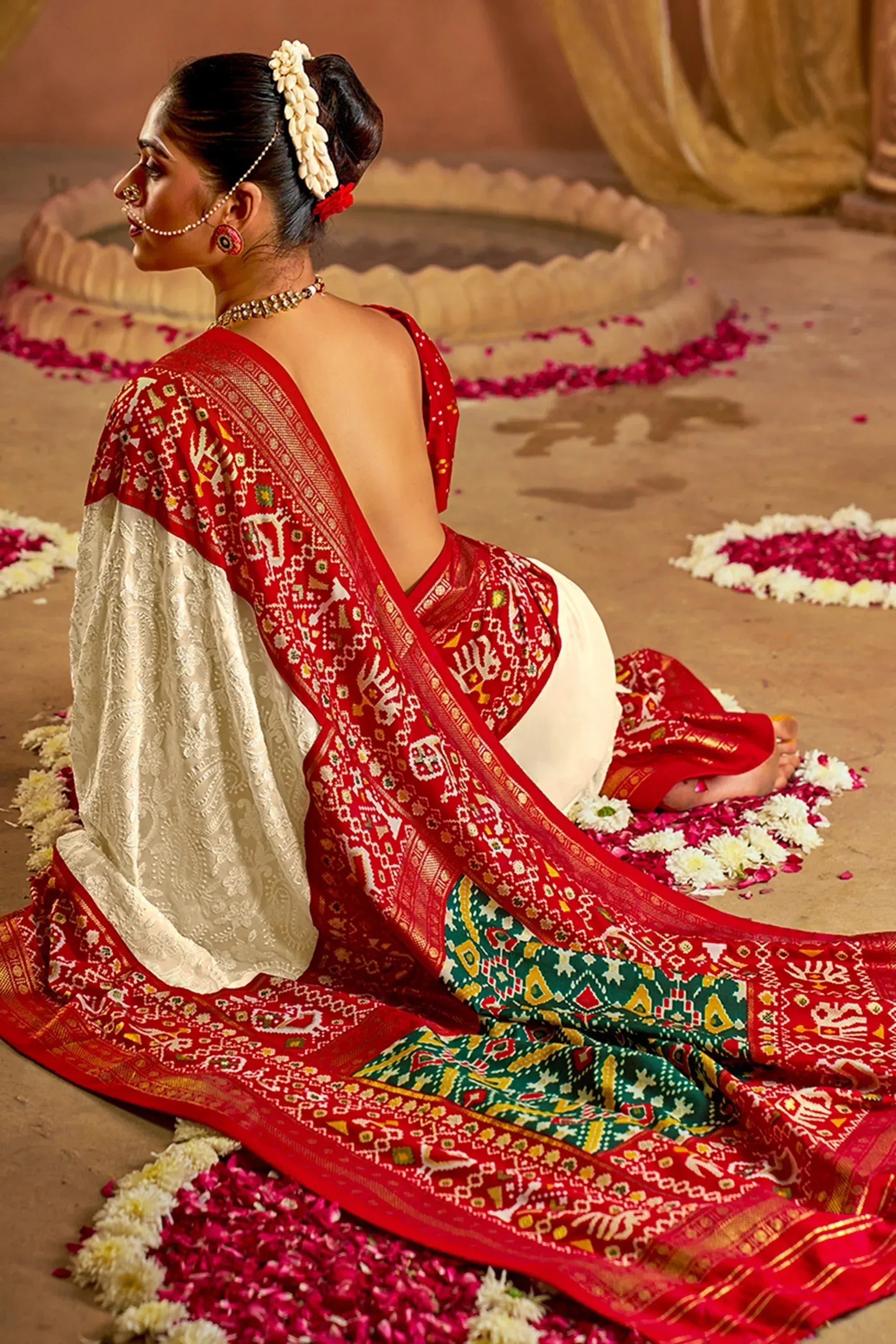 Woman in red and white ethnic saree with intricate embroidery, floral hair accessory, seated on flower petals