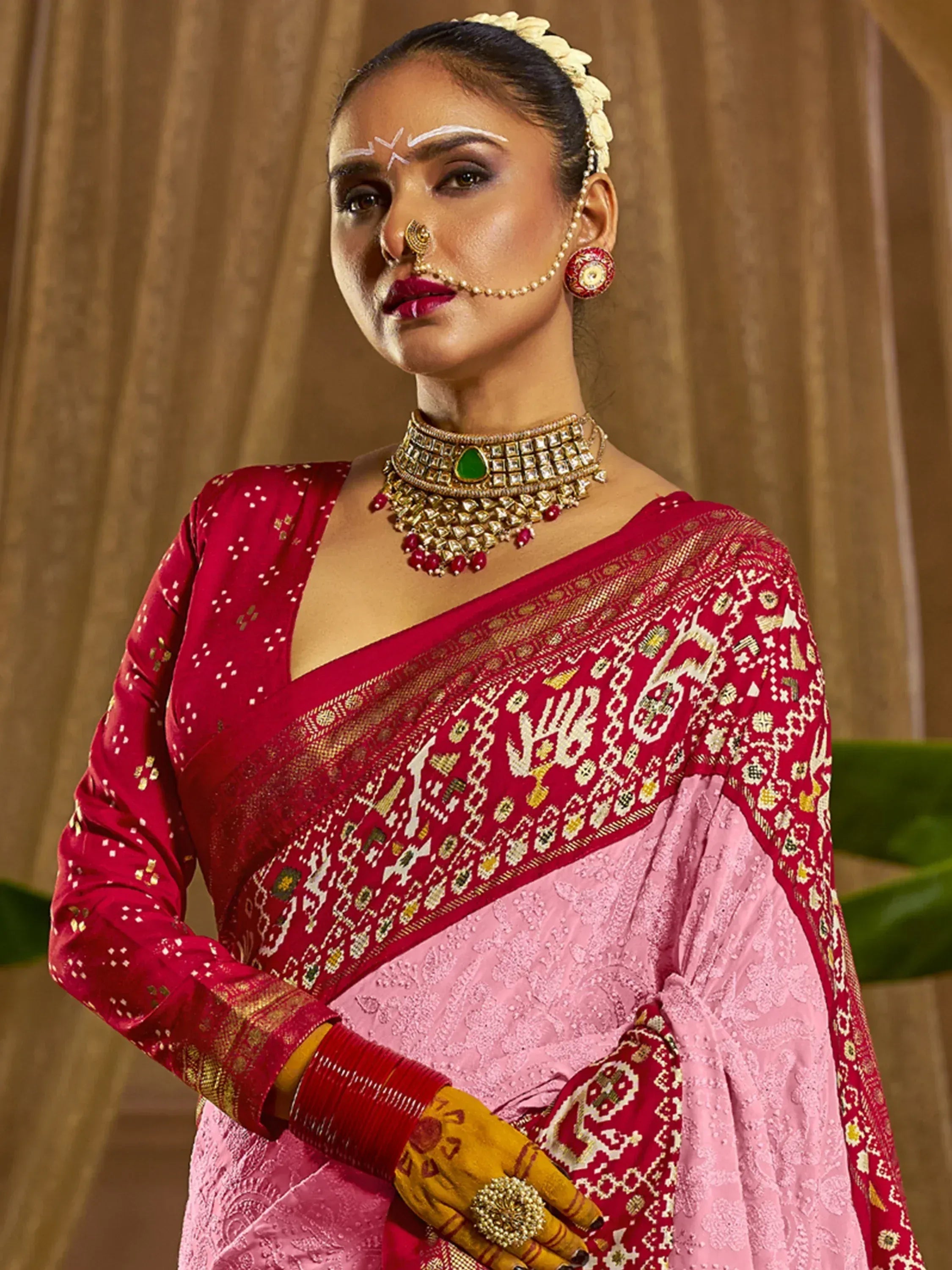 Woman in red and pink ethnic saree with gold embroidery, traditional jewelry, and floral hair accessory