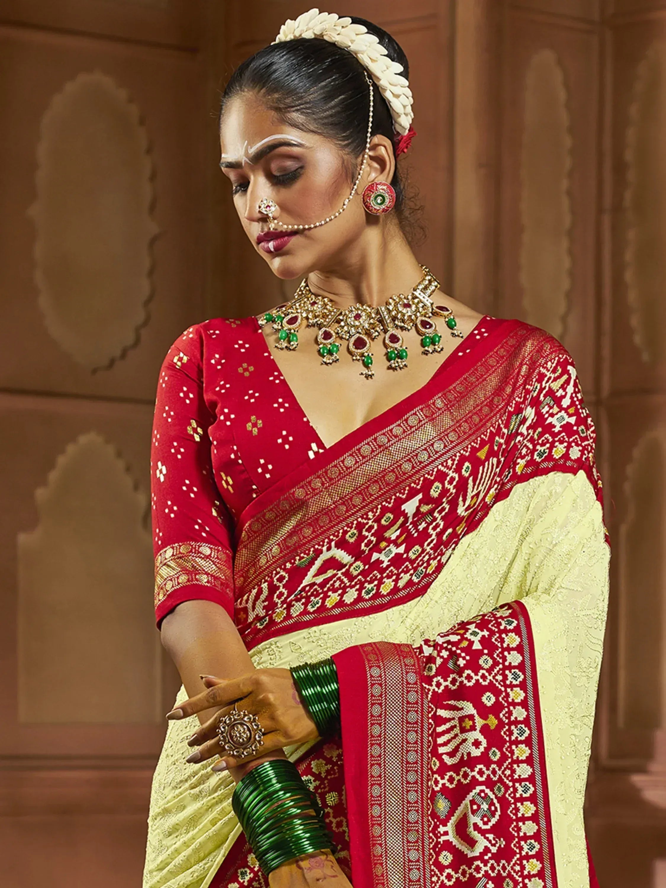 Red and cream embroidered saree with traditional Indian jewelry and floral hair accessory