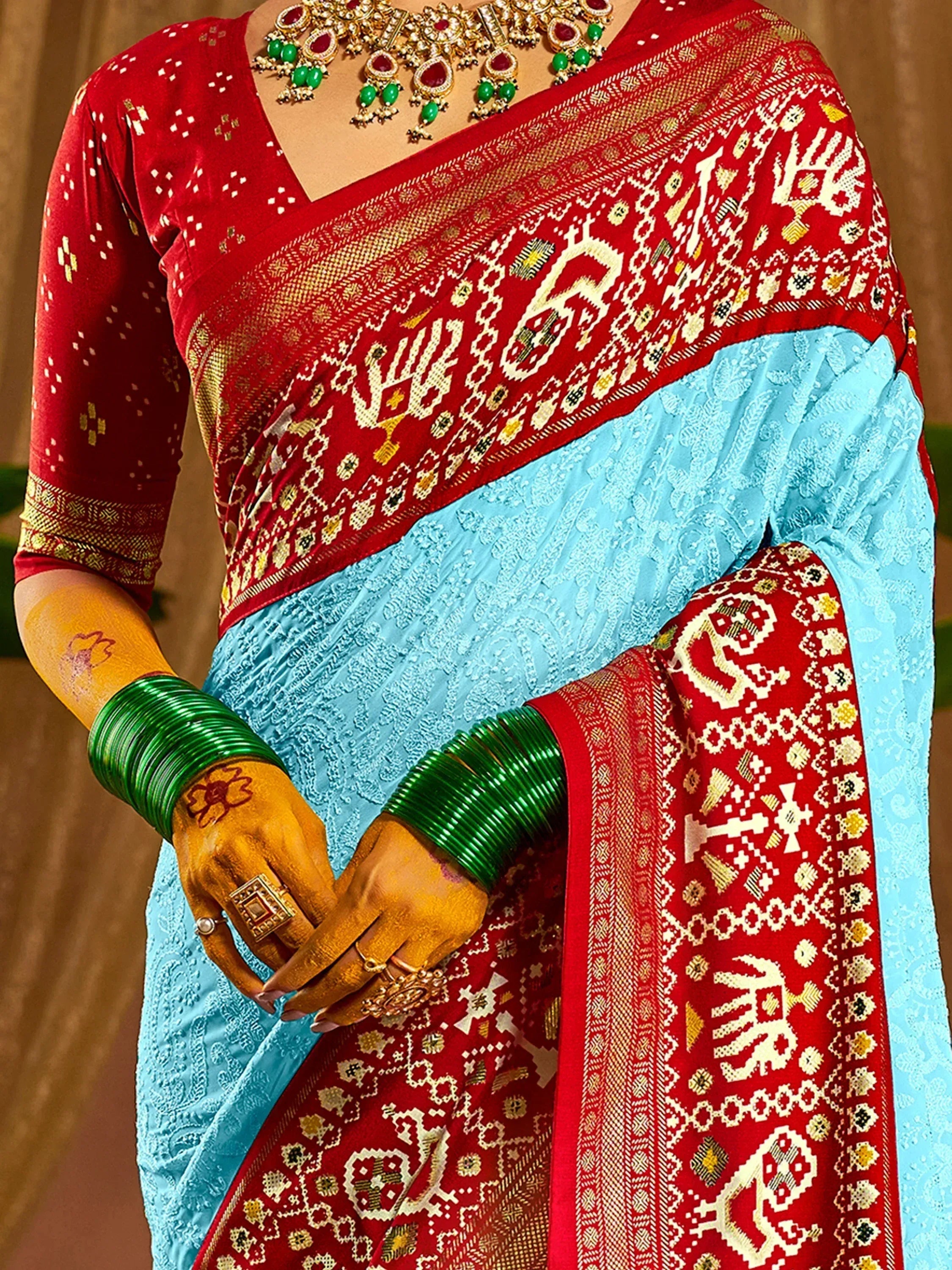 Red and blue ethnic saree with intricate patterns, paired with green bangles and traditional jewelry