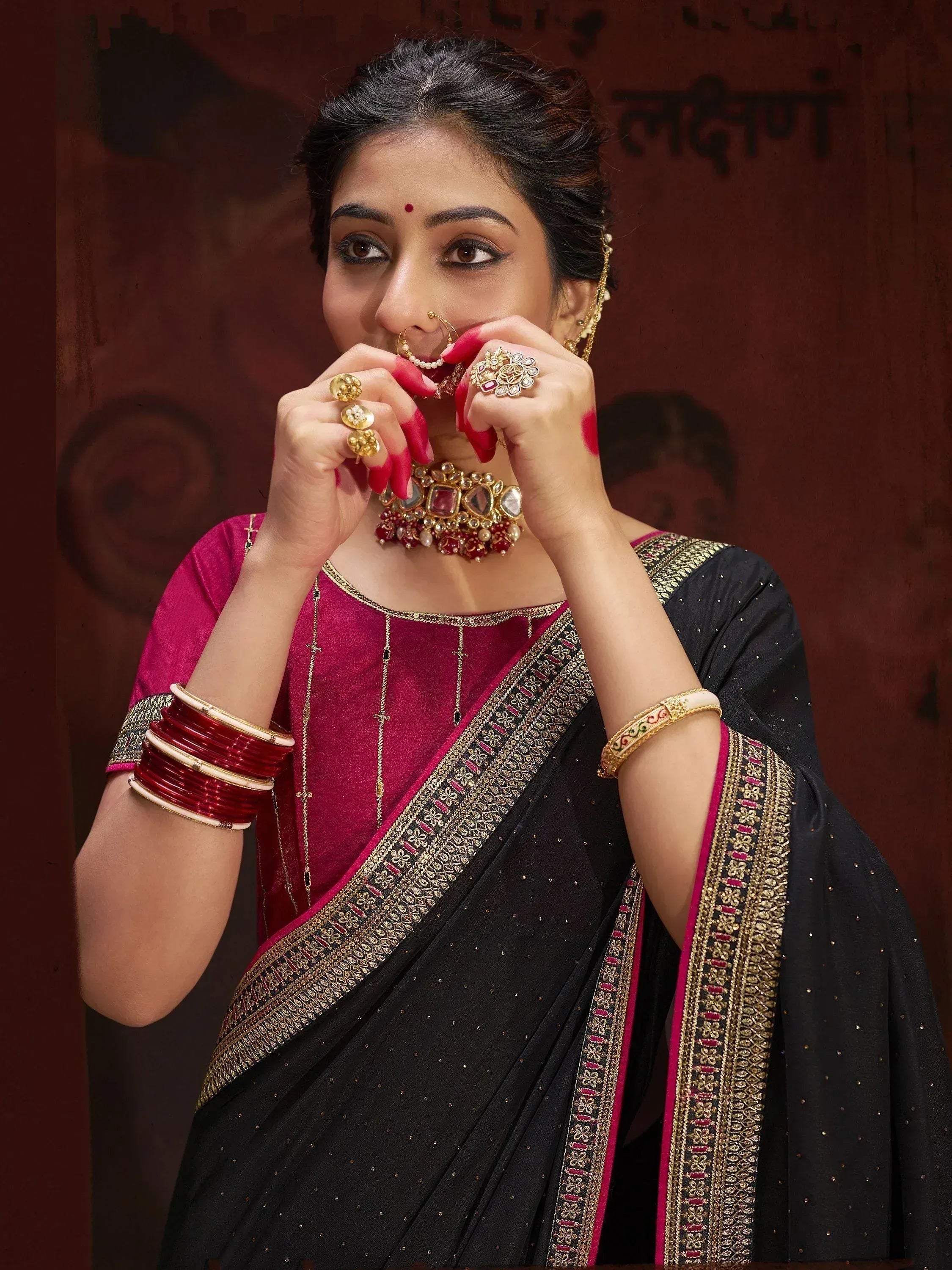 Woman in black and pink saree with gold embroidery, traditional Indian jewelry, and red bangles.
