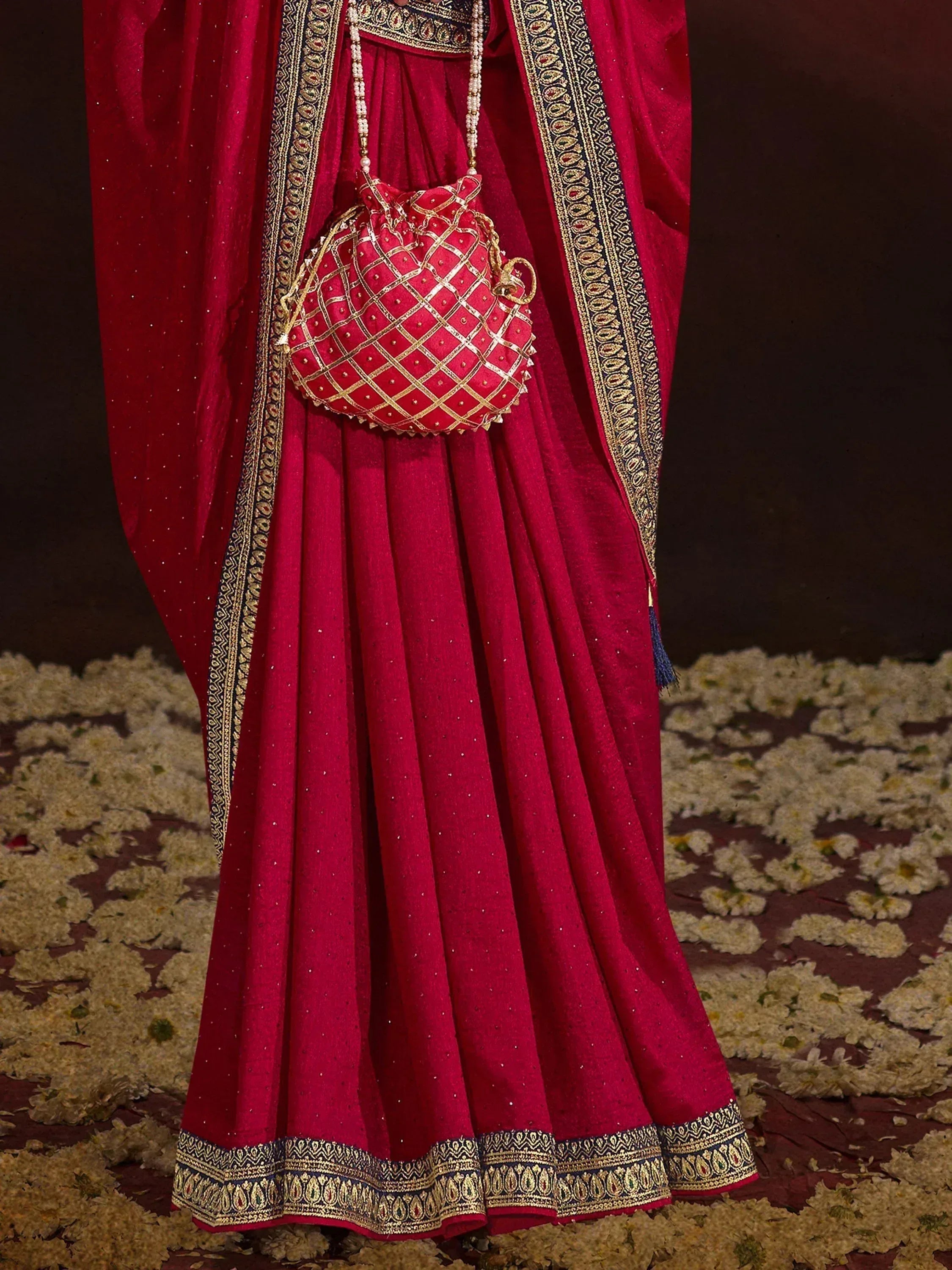 Red ethnic lehenga choli with gold embroidery, matching potli bag, and floral floor decor