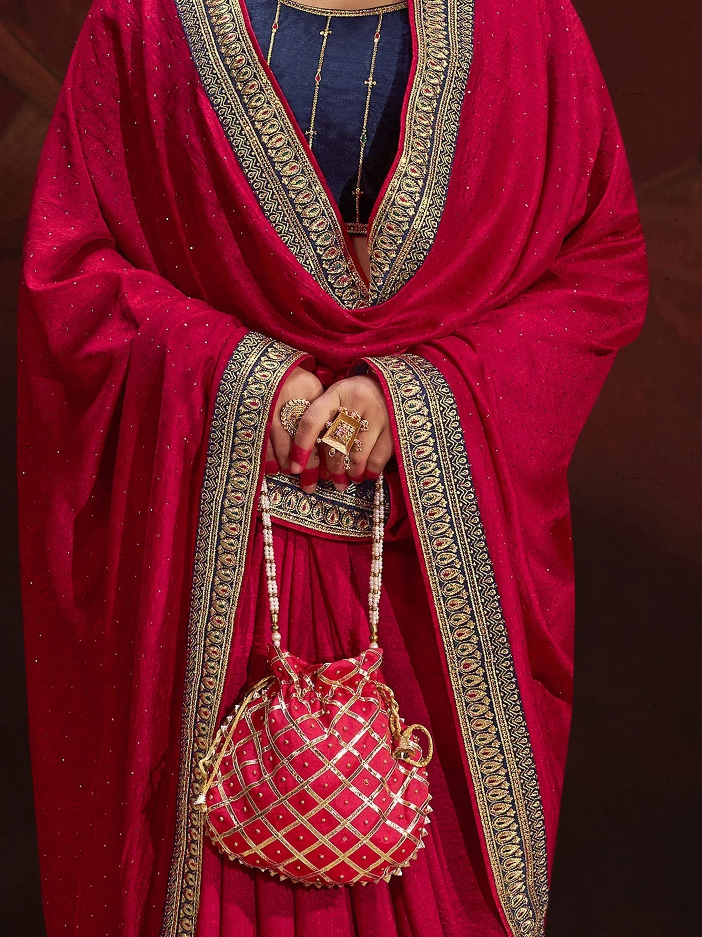 Red velvet ethnic gown with gold embroidery, matching potli bag, and traditional jewelry for Indian wear