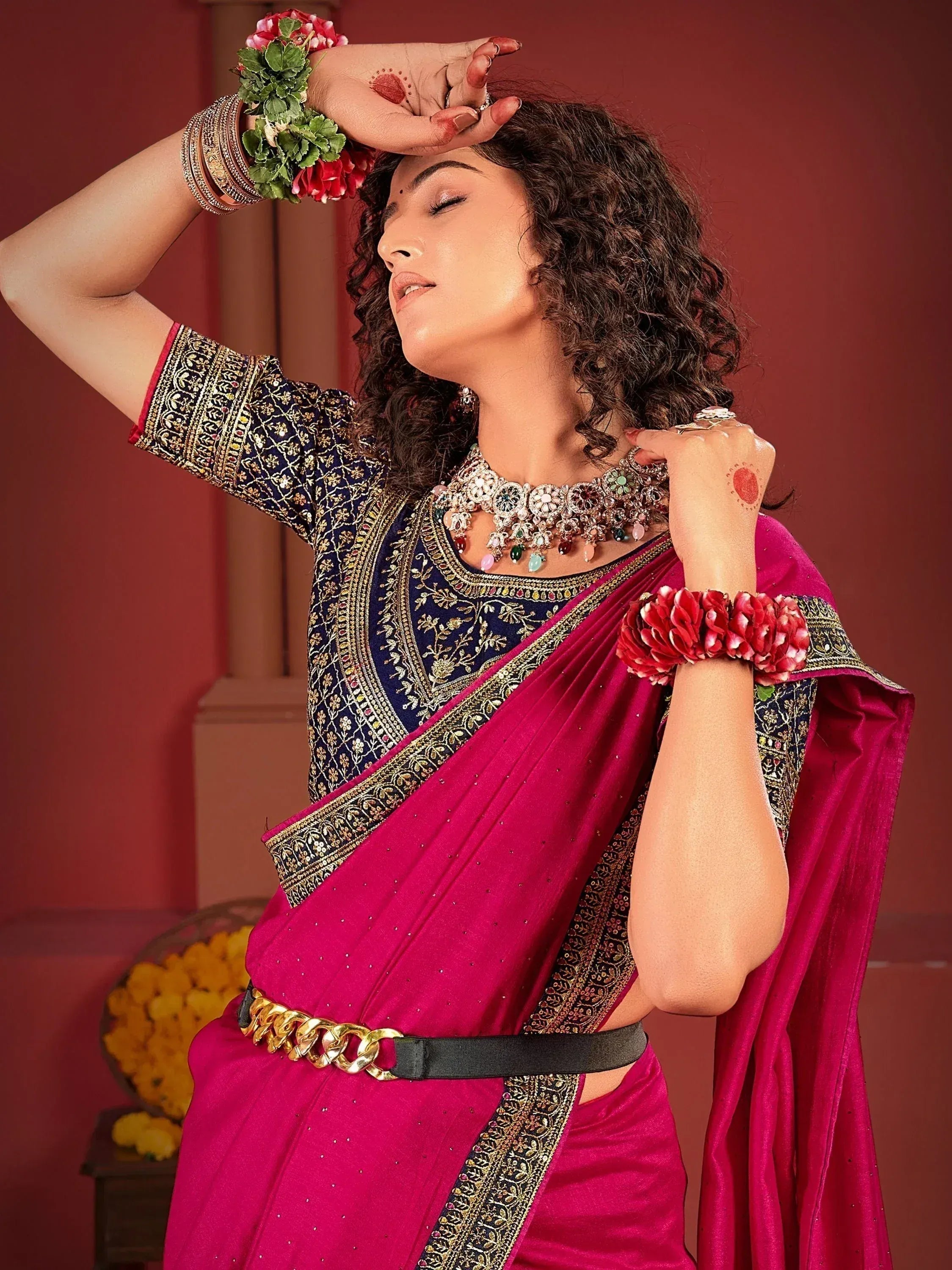 Woman in vibrant pink saree with navy blue embroidered blouse, floral bangles, and statement jewelry