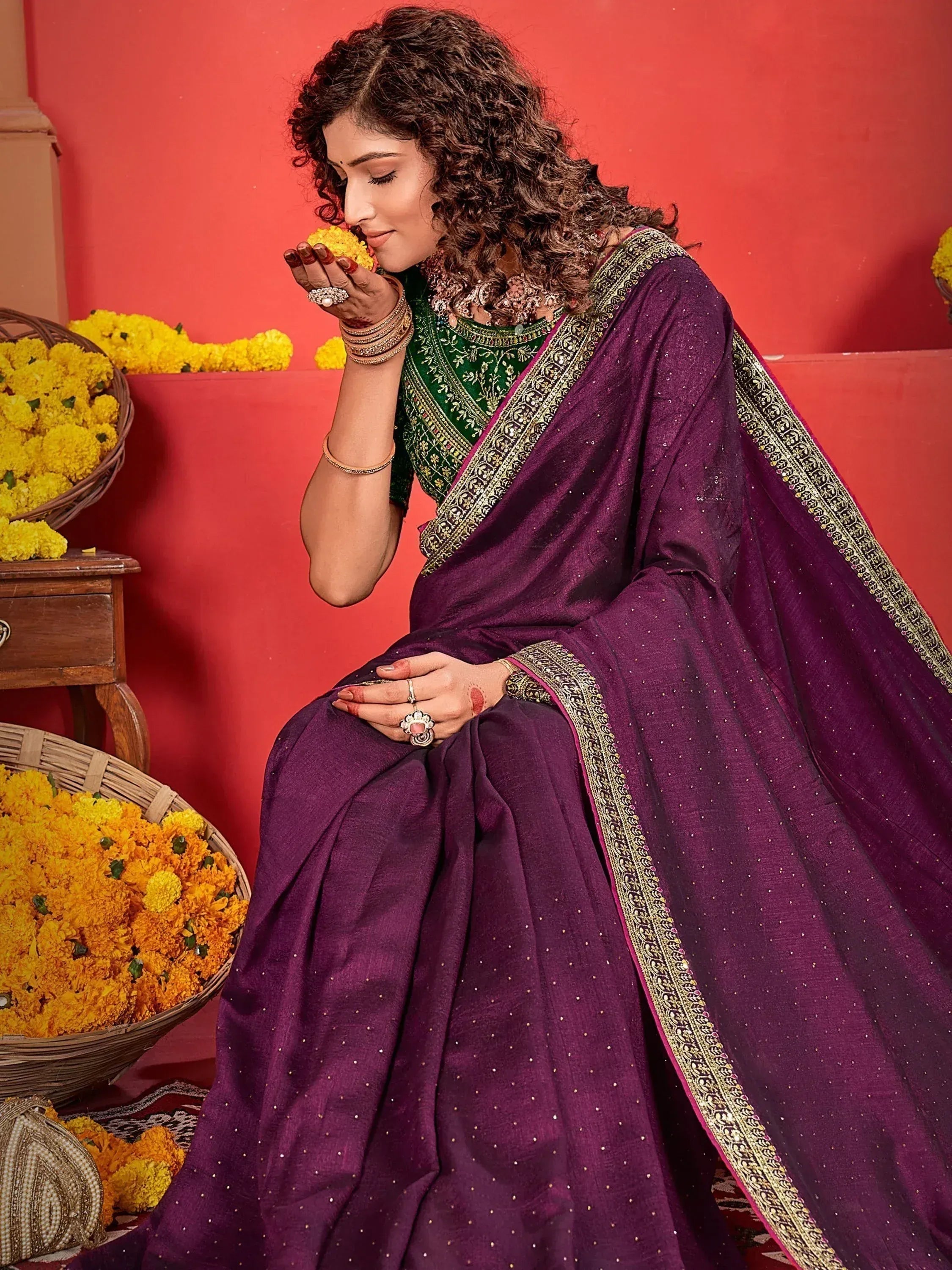 Woman in purple embroidered saree with green blouse, holding marigold flowers, festive ethnic wear