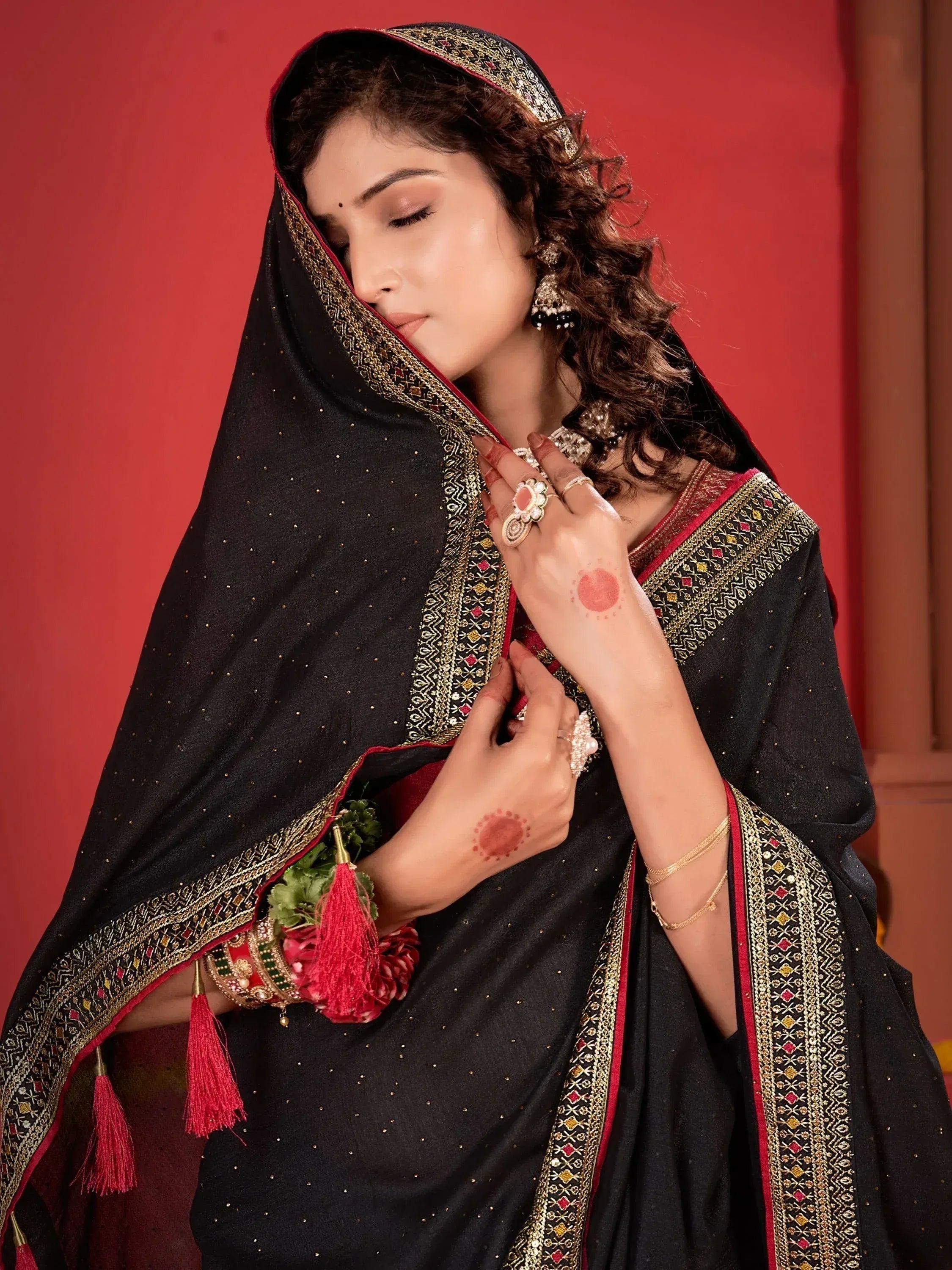 Elegant black ethnic saree with gold embroidery, red tassels, and traditional jewelry for festive occasions