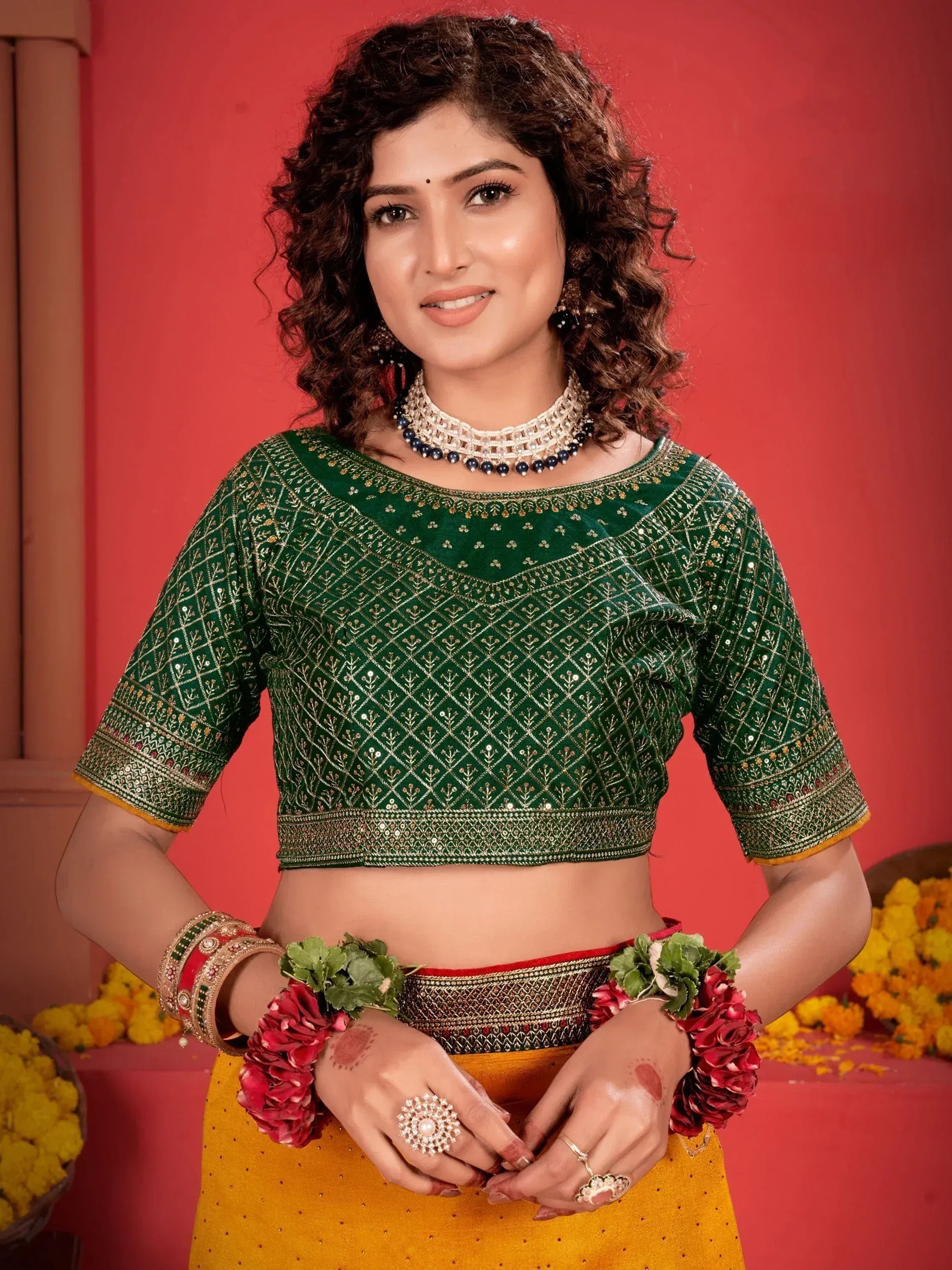 Woman in green embroidered blouse with gold detailing, floral wrist garlands, and traditional Indian jewelry
